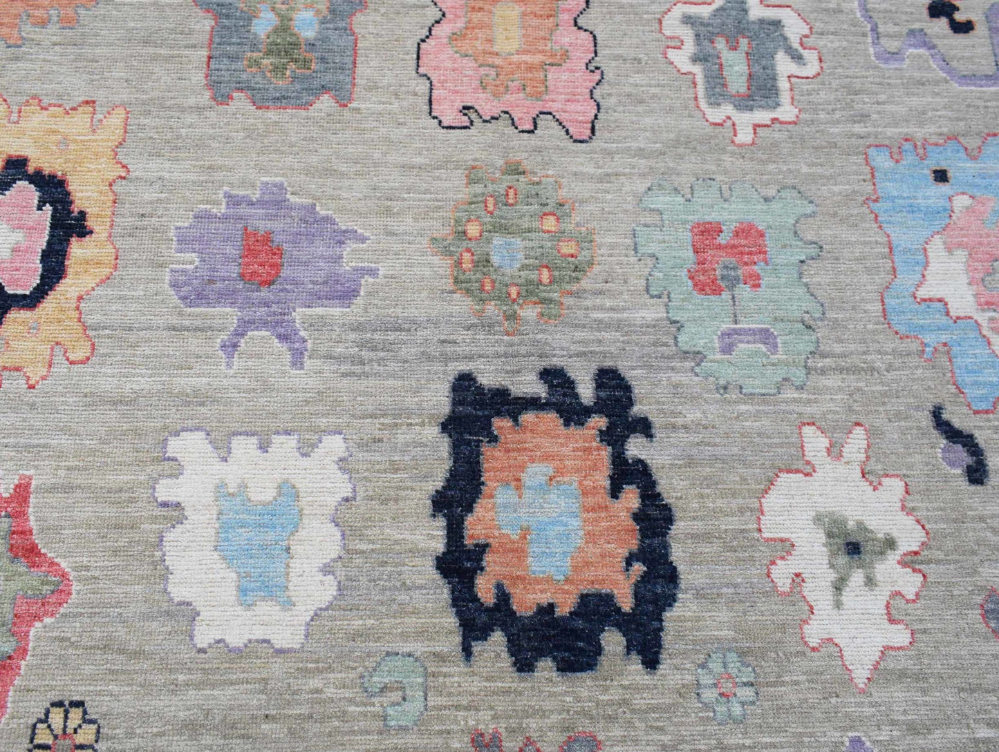 A handwoven transitional Oushak rug featuring colorful abstract floral motifs on a grey field.
