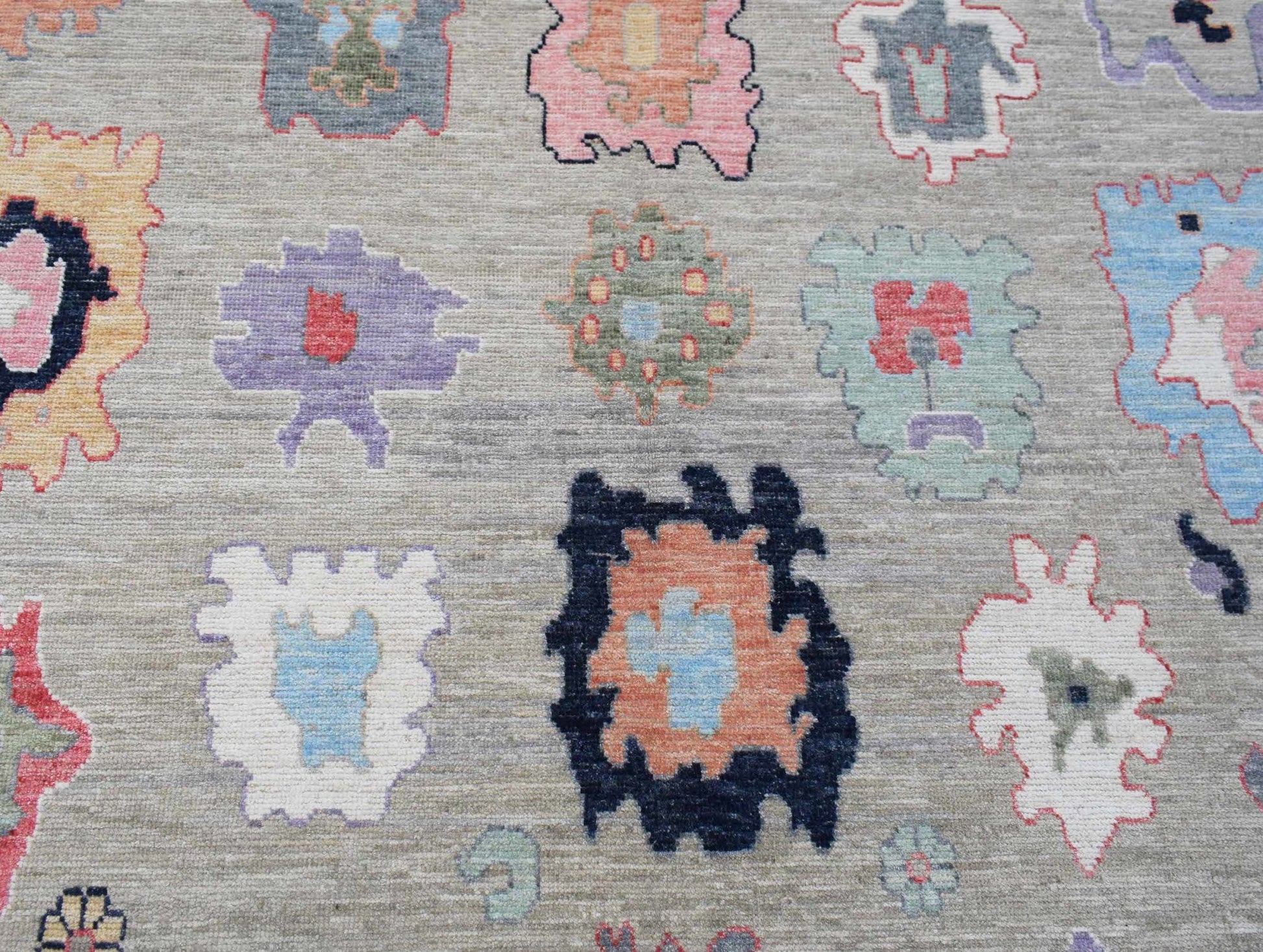 A handwoven transitional Oushak rug featuring colorful abstract floral motifs on a grey field.