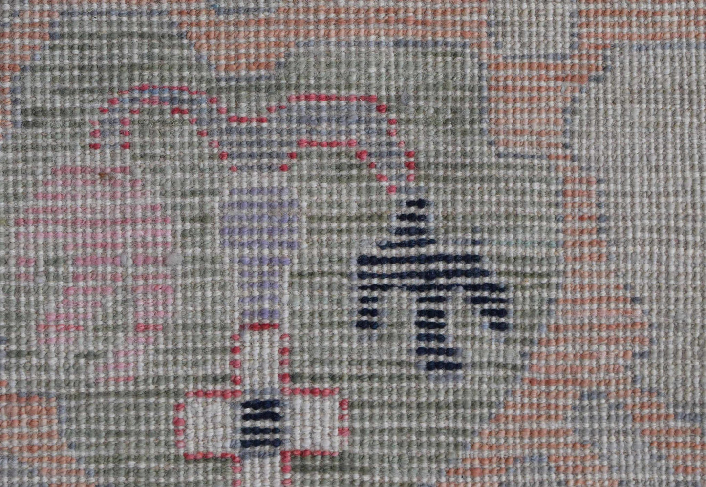 A close-up of a handwoven Oushak rug featuring a soft, muted pattern with geometric motifs.