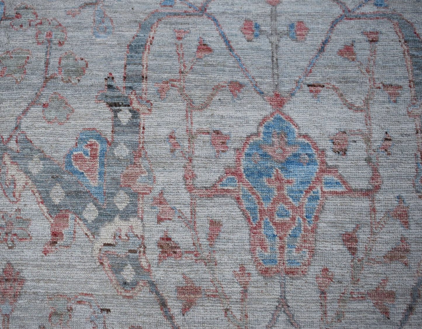 A handwoven transitional Oushak rug featuring a floral pattern in blue and red on a grey background.