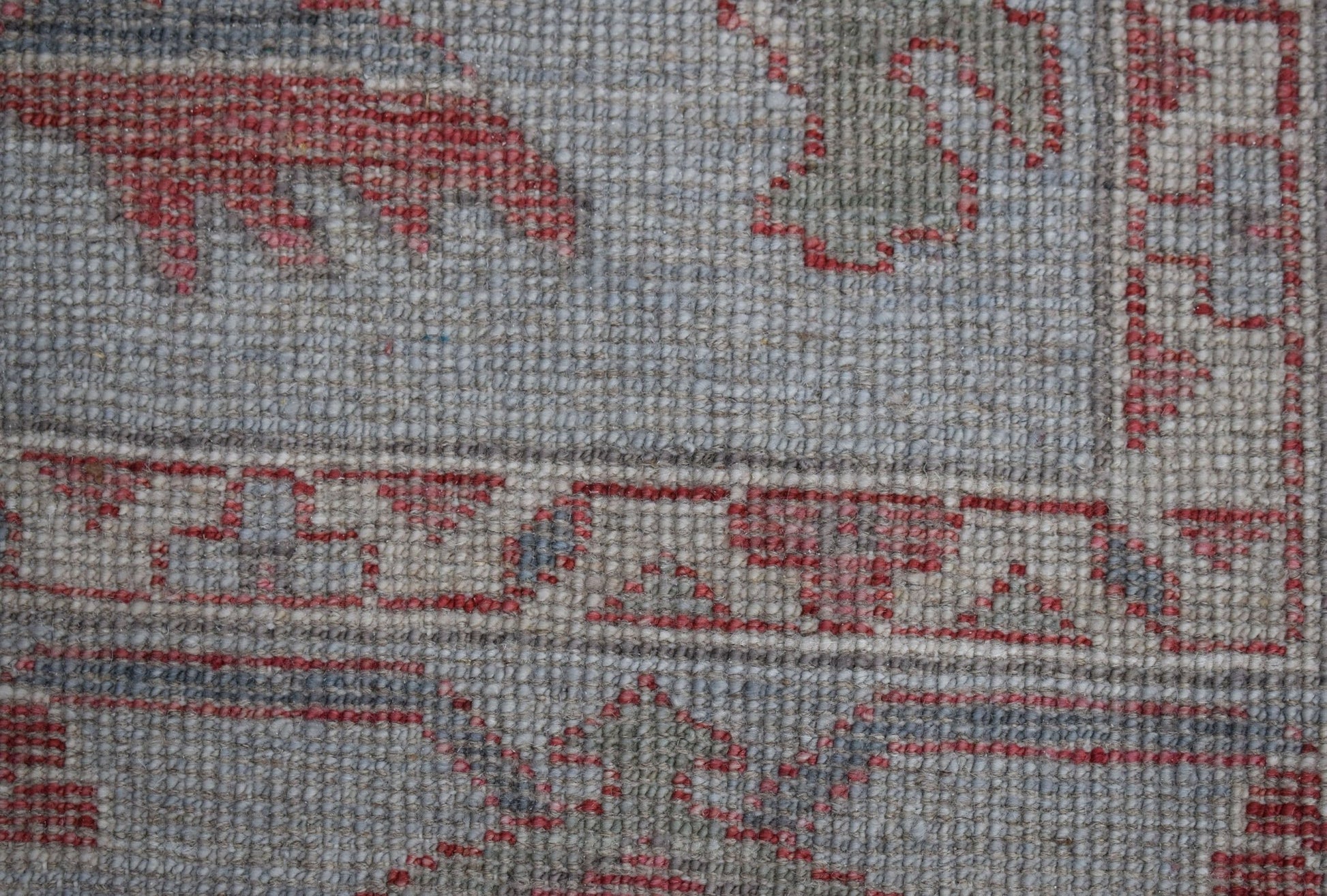 A close-up of a handwoven Oushak rug featuring a traditional floral pattern in red and grey tones.