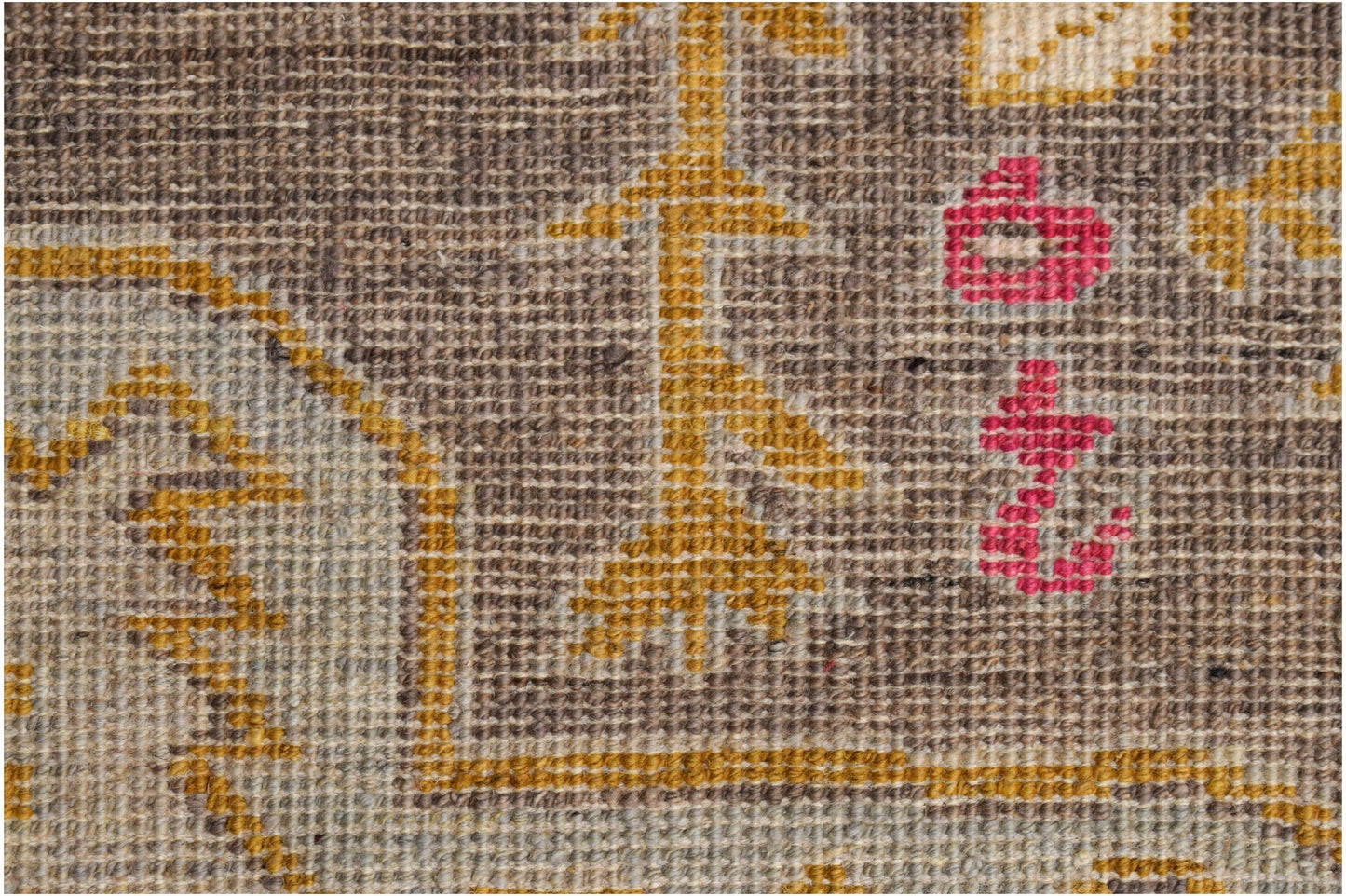 A close-up of a hand-knotted wool rug featuring geometric patterns in brown, gold, and pink.