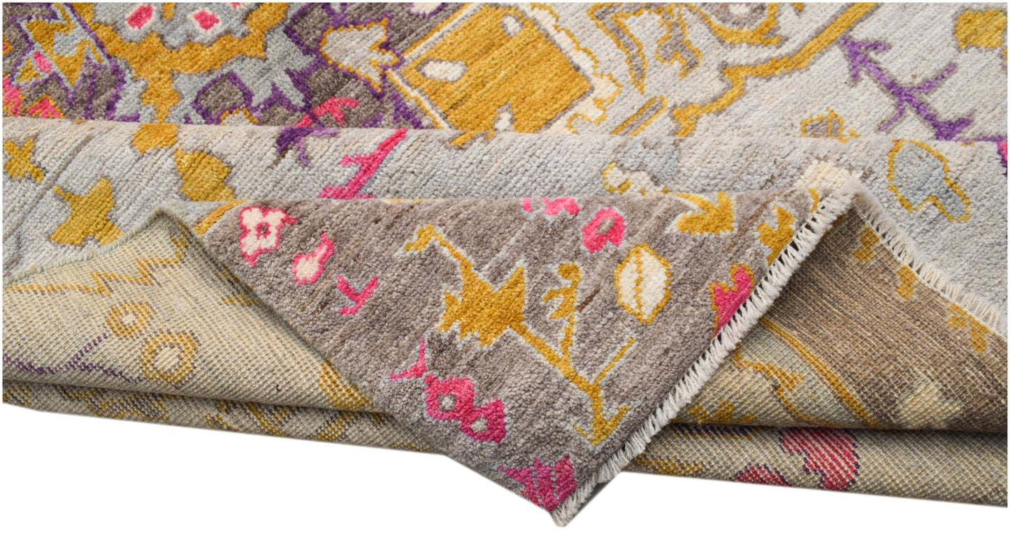 A hand-knotted wool rug featuring a transitional geometric pattern in grey, yellow, and pink.