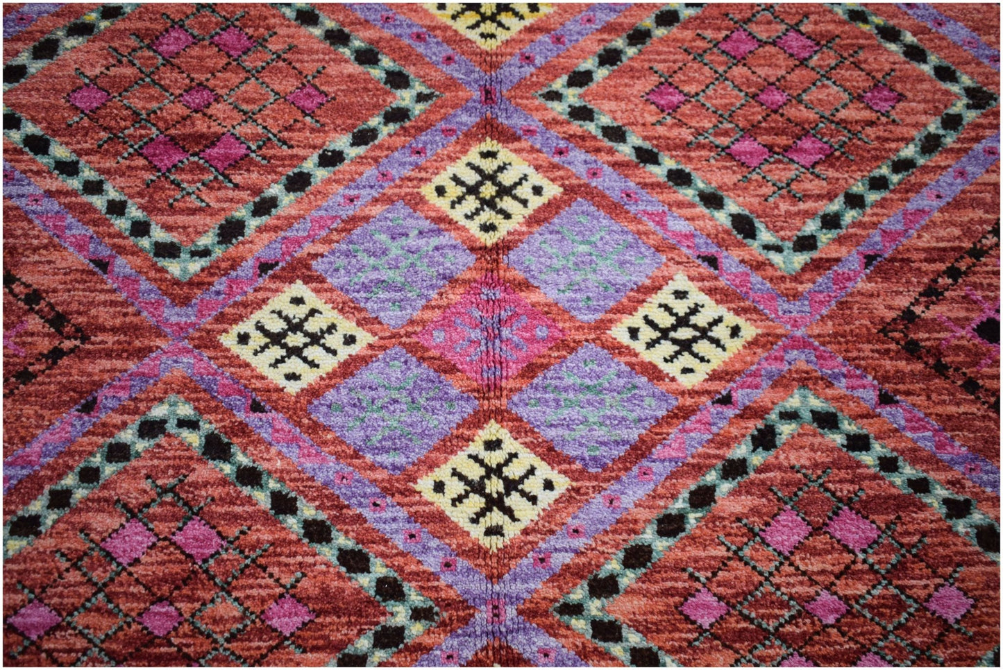 A hand-knotted wool rug featuring a vibrant geometric pattern in red, purple, and yellow.