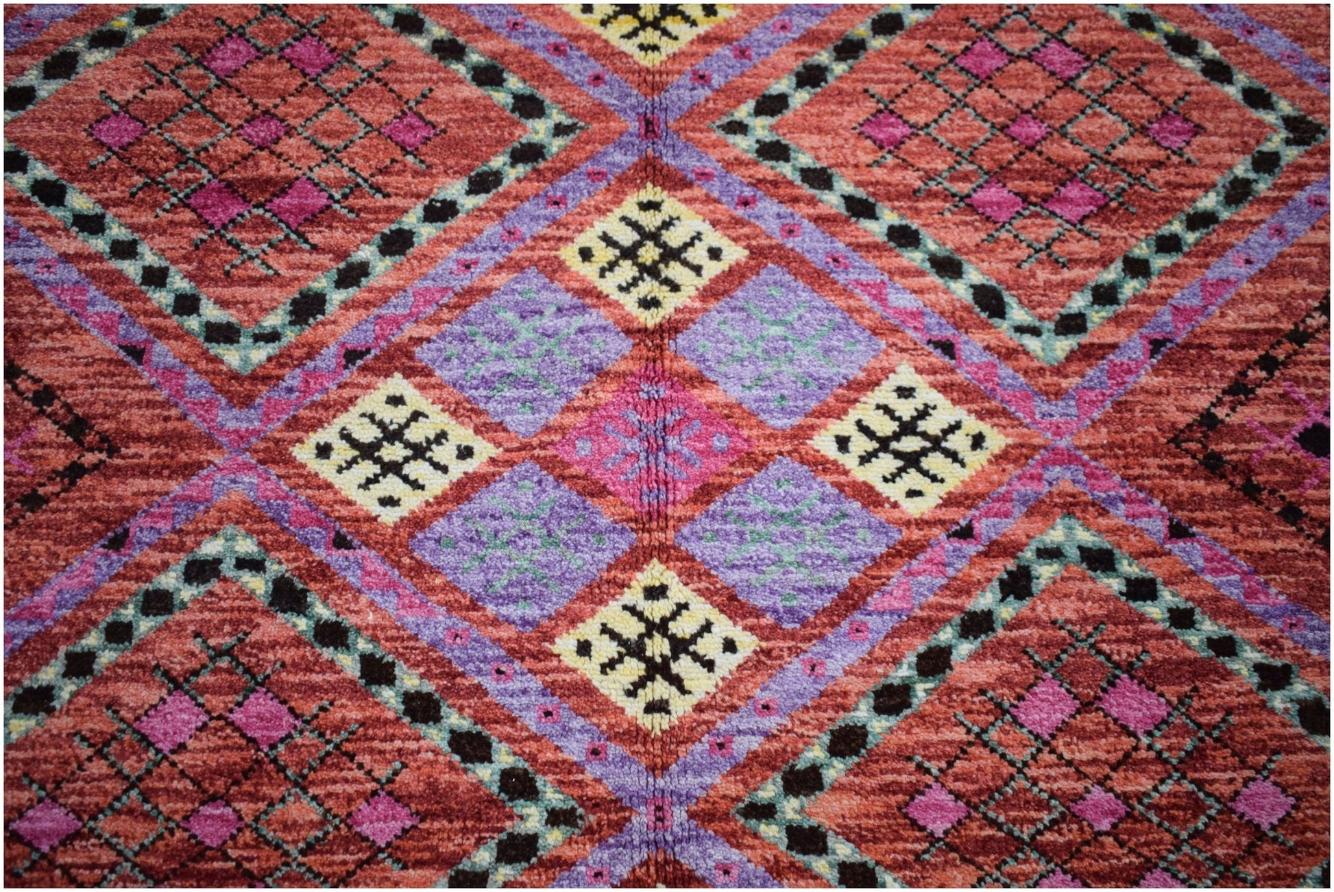 A hand-knotted wool rug featuring a vibrant geometric pattern in red, purple, and yellow.