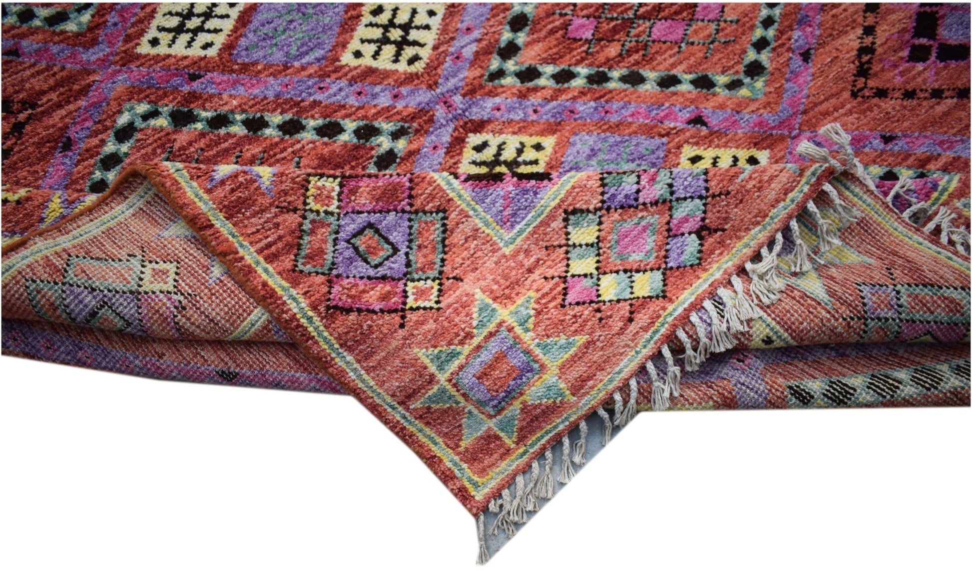 A hand-knotted wool rug featuring a vibrant geometric pattern in shades of red, purple, and yellow.
