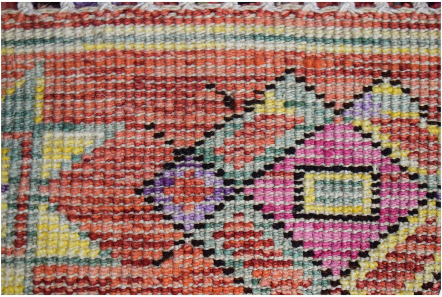 A close-up of a hand-knotted wool rug featuring geometric patterns in orange, pink, and yellow.