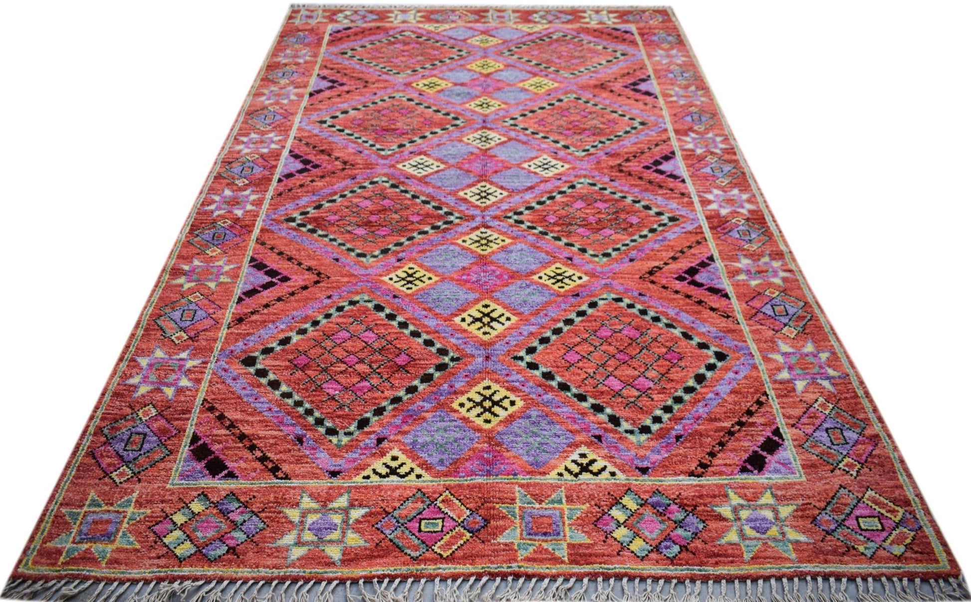 A hand-knotted wool rug featuring a vibrant geometric diamond pattern in red, purple, and yellow.