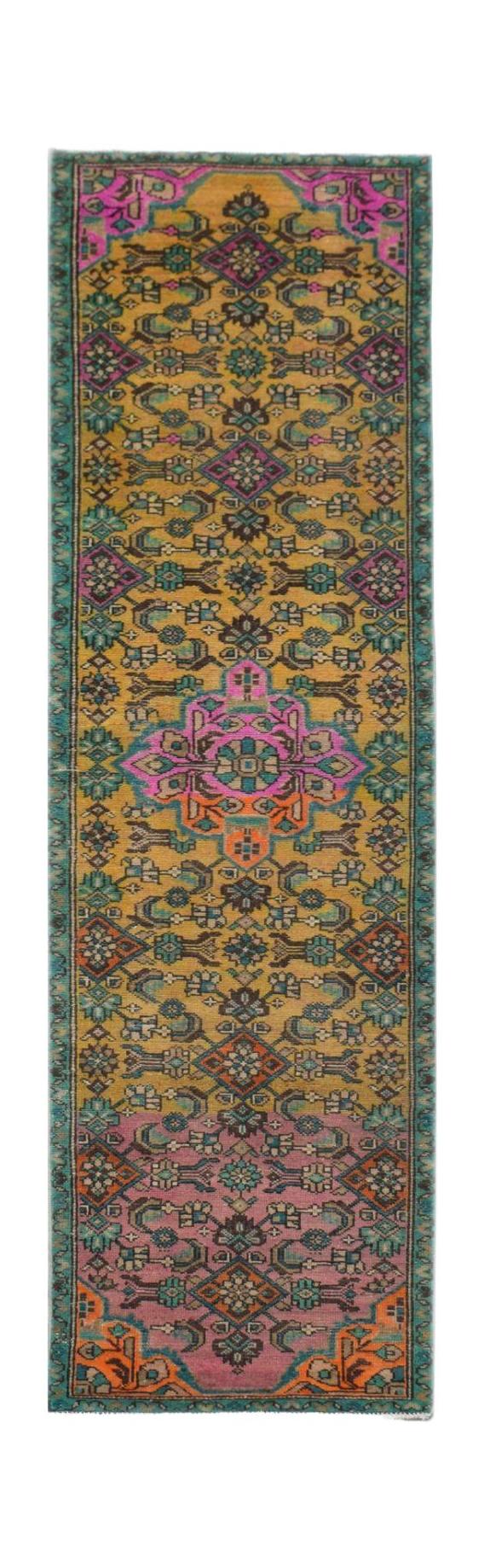 A vintage Persian runner rug featuring a vibrant geometric pattern in shades of gold, pink, and teal.