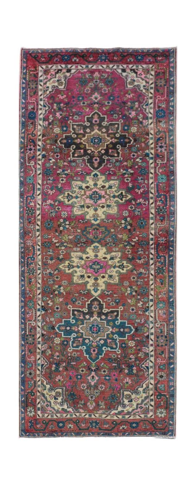 A vintage handmade Persian runner rug featuring a floral medallion pattern in pink and red tones.