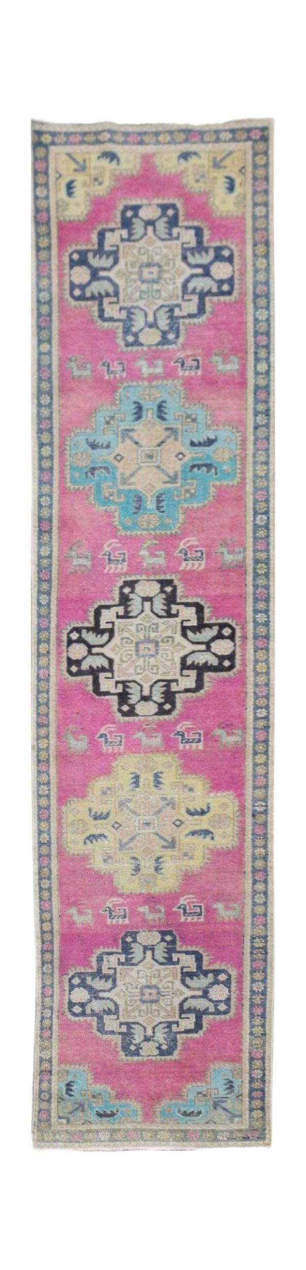 A handmade vintage Persian runner rug featuring geometric medallions on a vibrant pink background.