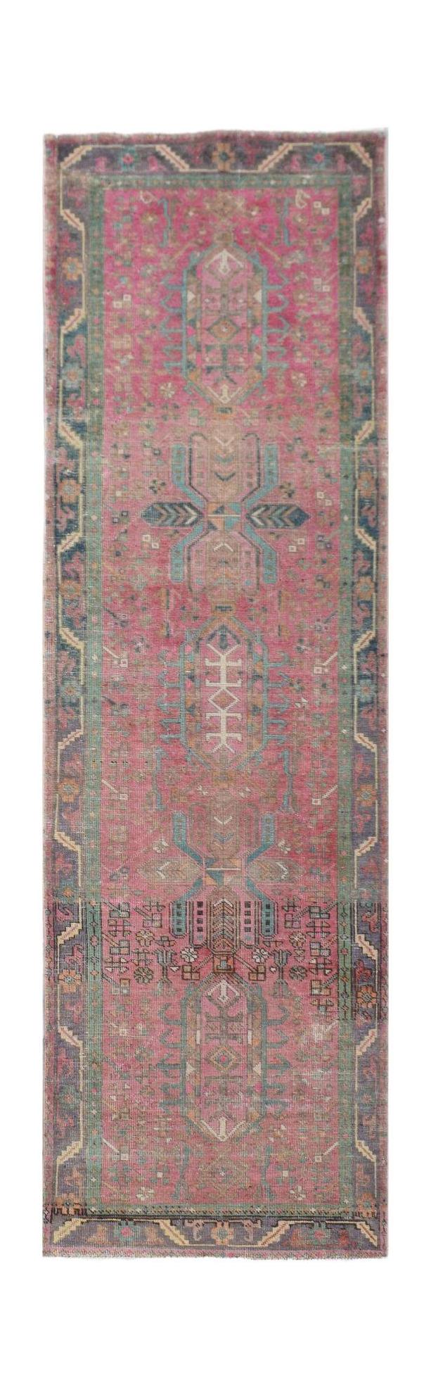 A vintage Persian runner rug featuring a vibrant pink field with intricate blue and cream patterns.