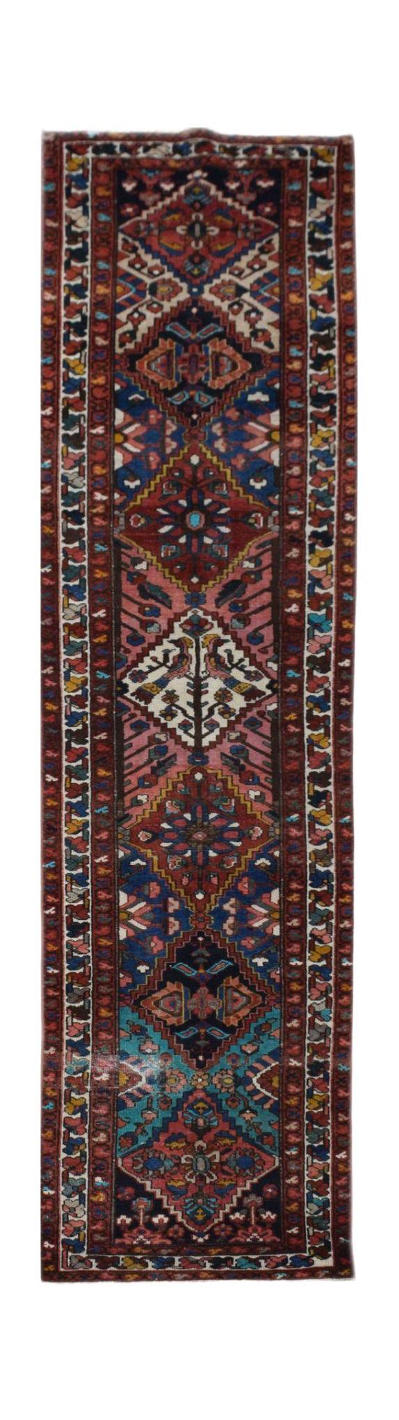 A vintage Persian runner rug featuring a geometric tribal pattern in red, blue, and cream tones.