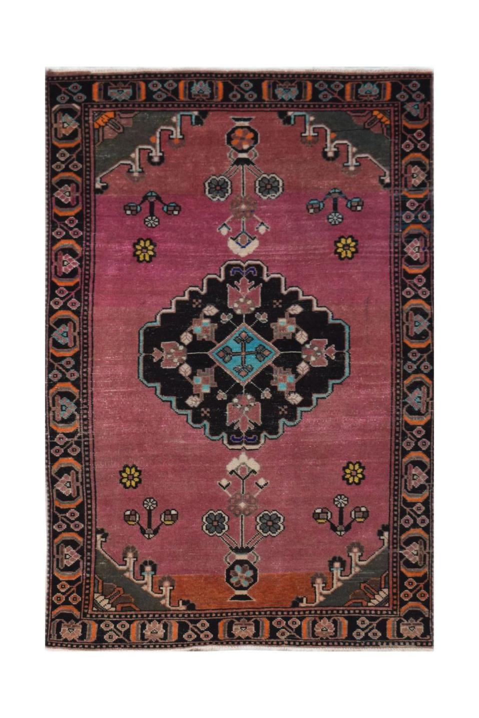 A handmade vintage Persian wool rug featuring a central black medallion on a pink field.