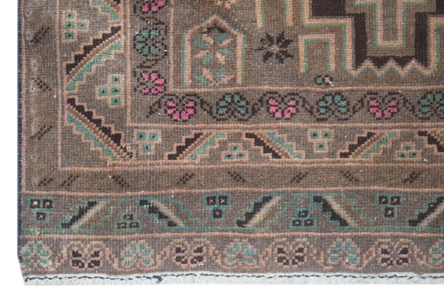 A close-up of a vintage Afghan Baluch runner featuring geometric patterns in brown, green, and pink.