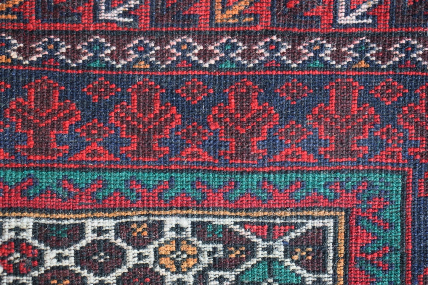 A close-up of a vintage Afghan Baluch rug featuring intricate geometric patterns in red and blue.