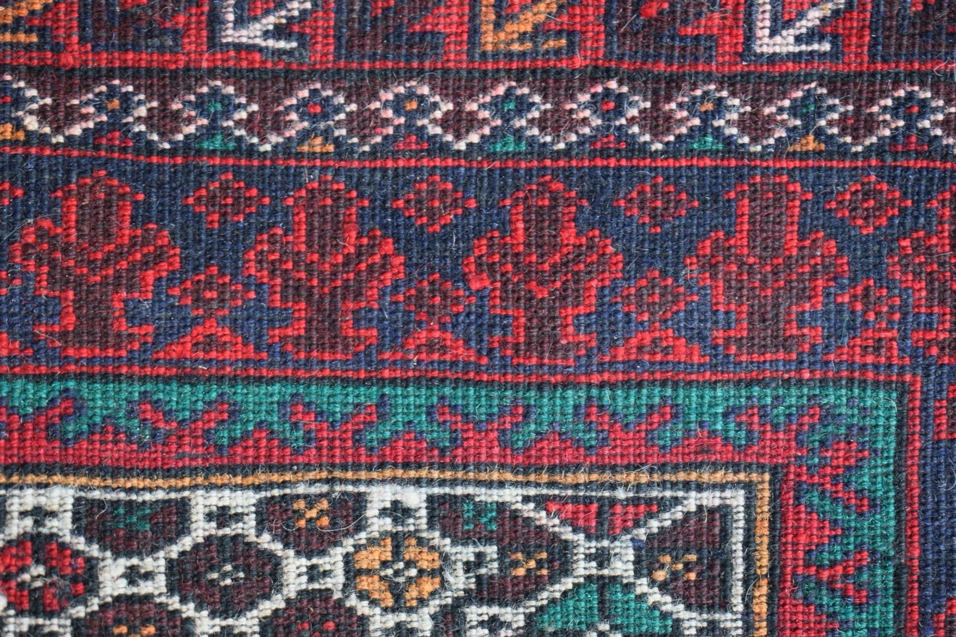 A close-up of a vintage Afghan Baluch rug featuring intricate geometric patterns in red and blue.