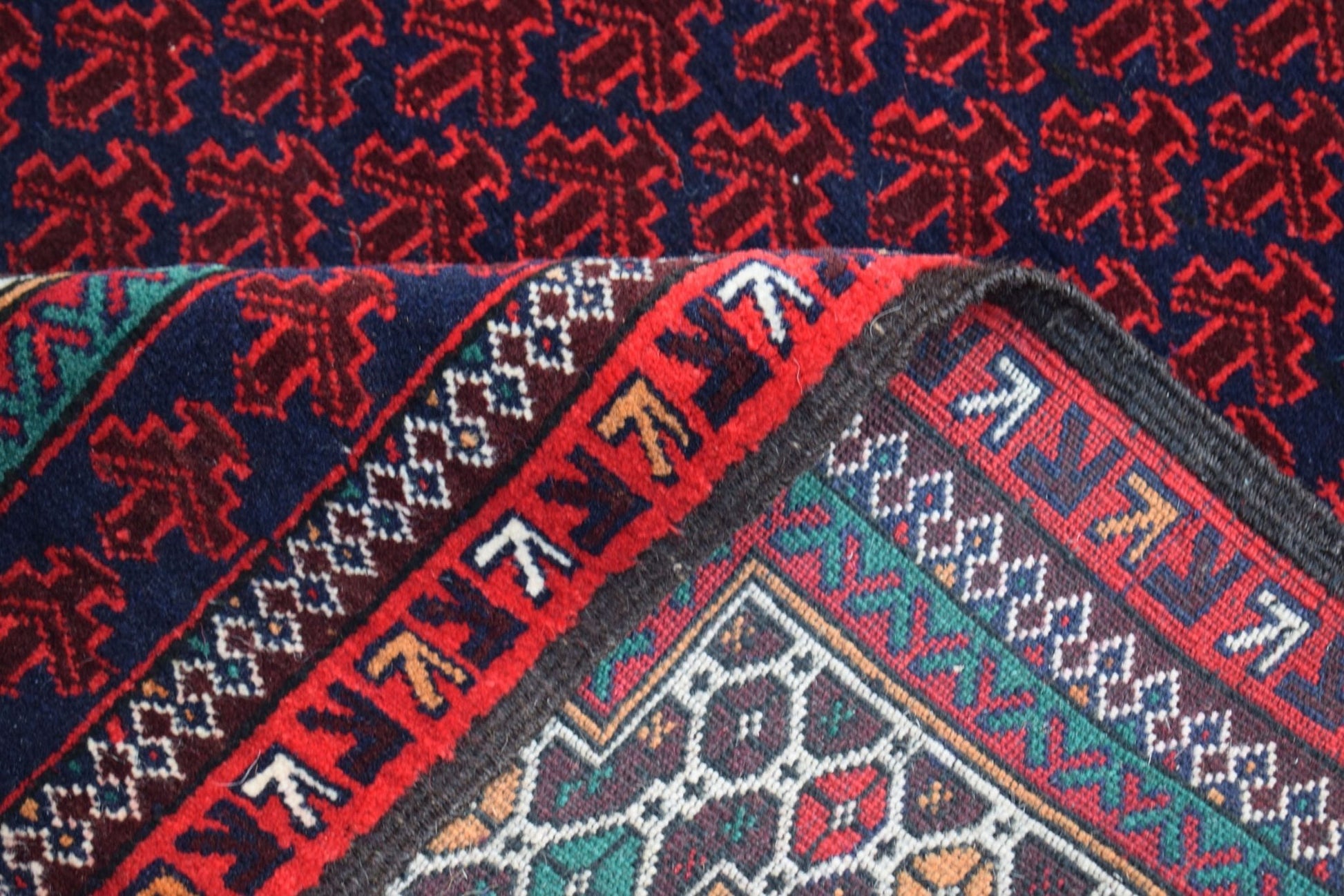 A vintage handmade Afghan Baluch rug featuring a dark blue field with red geometric motifs.