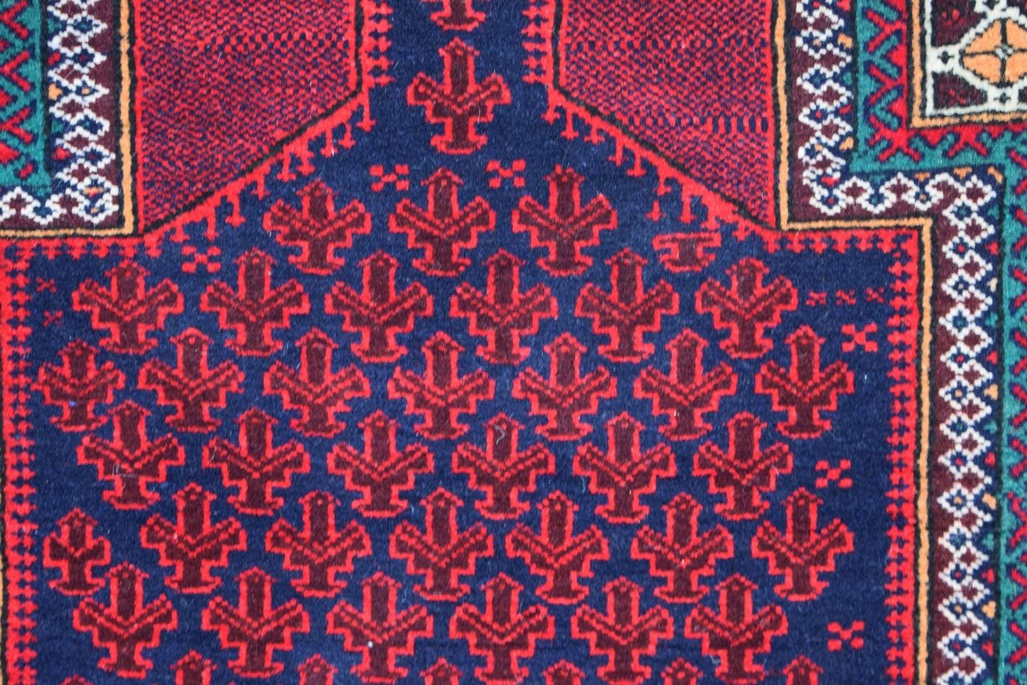 A vintage Afghan Baluch rug featuring a repeating red geometric motif on a dark blue background.