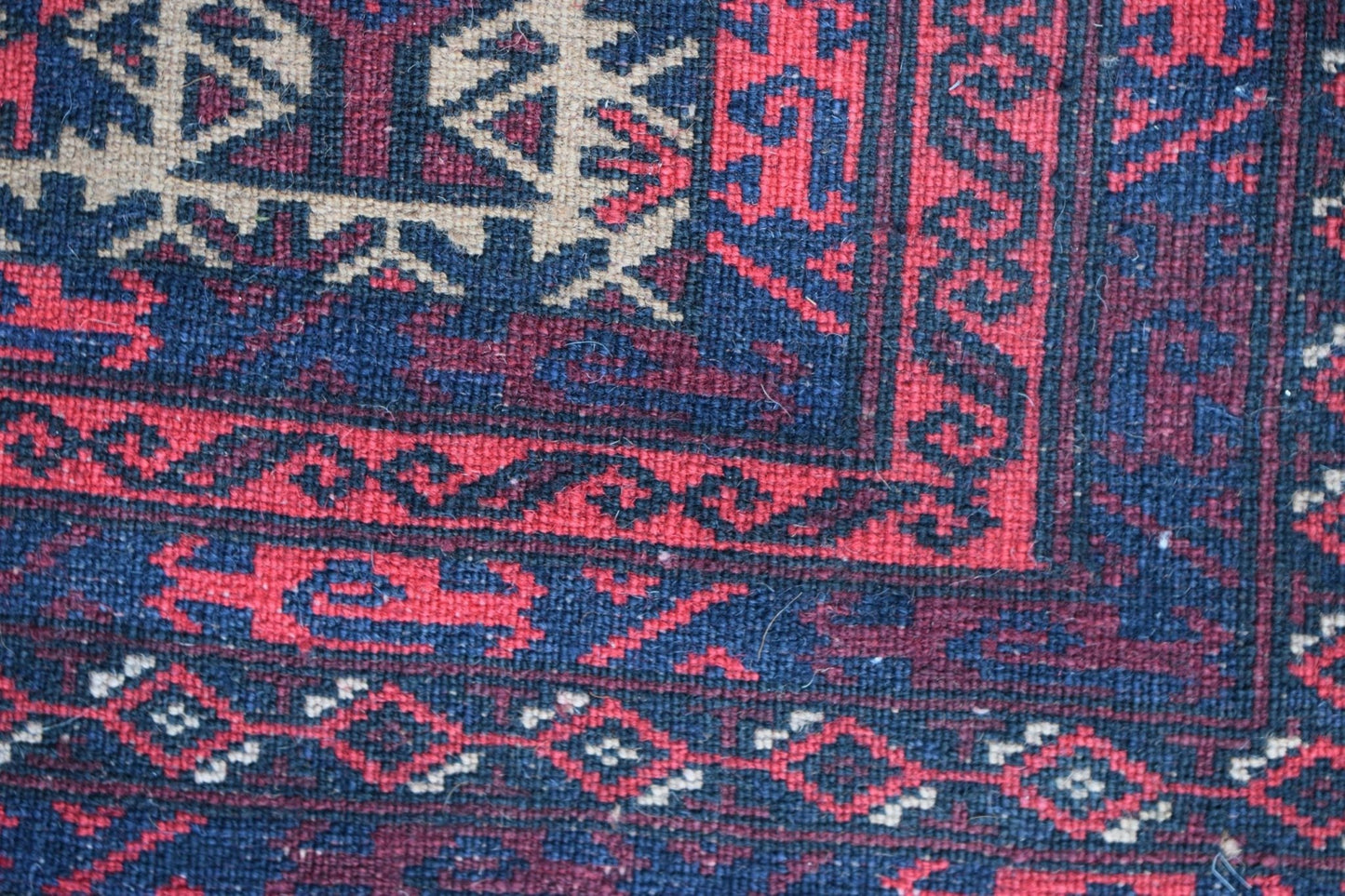 A close-up of a vintage Afghan Baluch rug featuring geometric patterns in red, blue, and ivory.