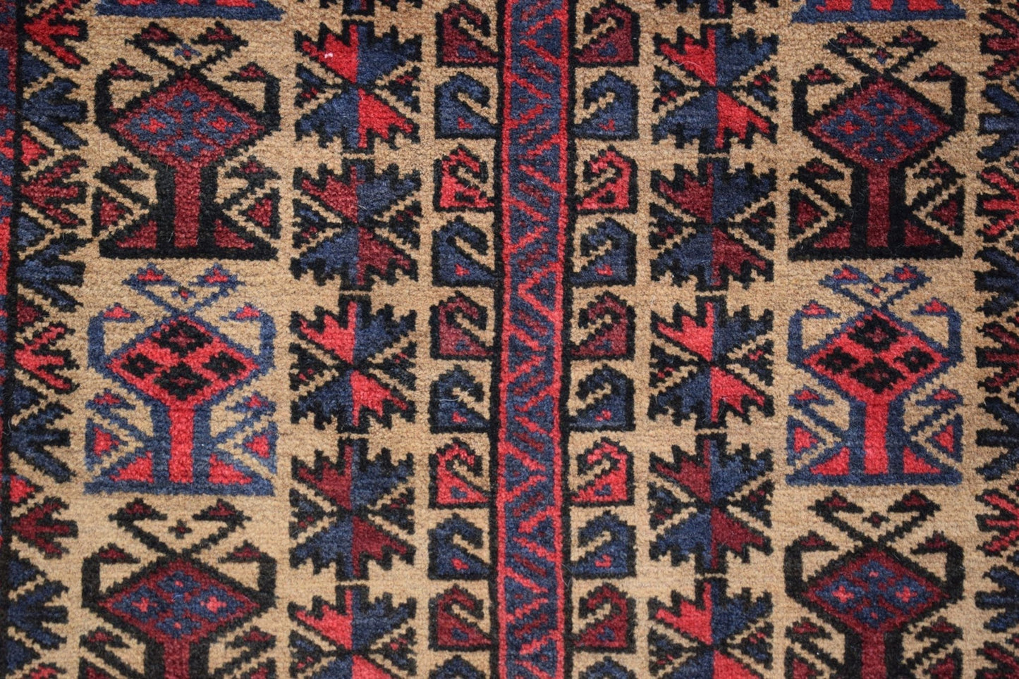 A vintage Afghan Baluch rug featuring geometric tribal patterns in red, blue, and brown wool.