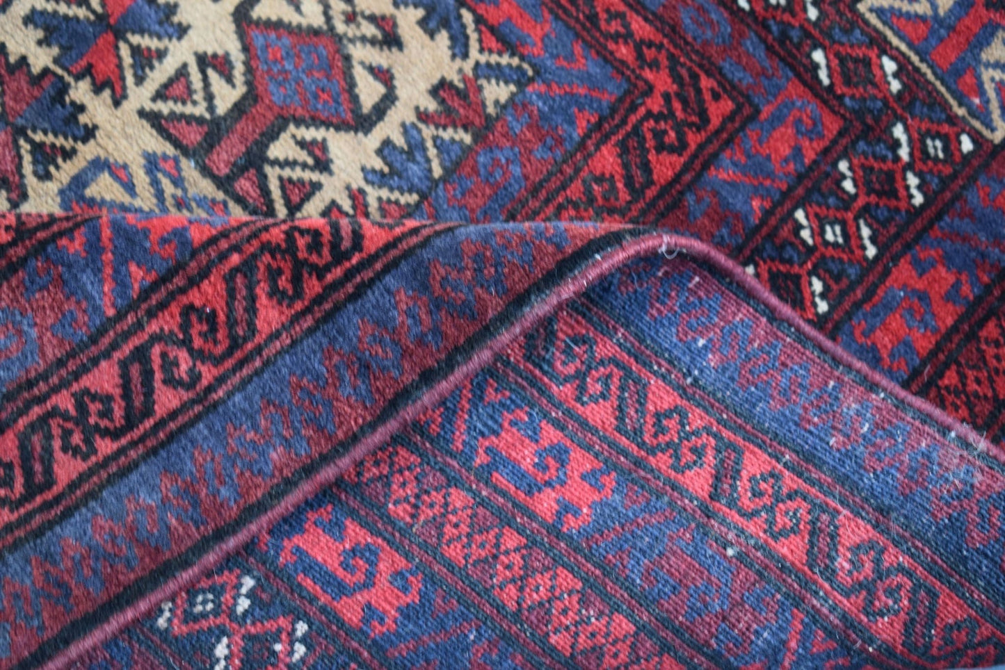 A folded vintage Afghan Baluch rug featuring geometric patterns in deep red, blue, and ivory wool.