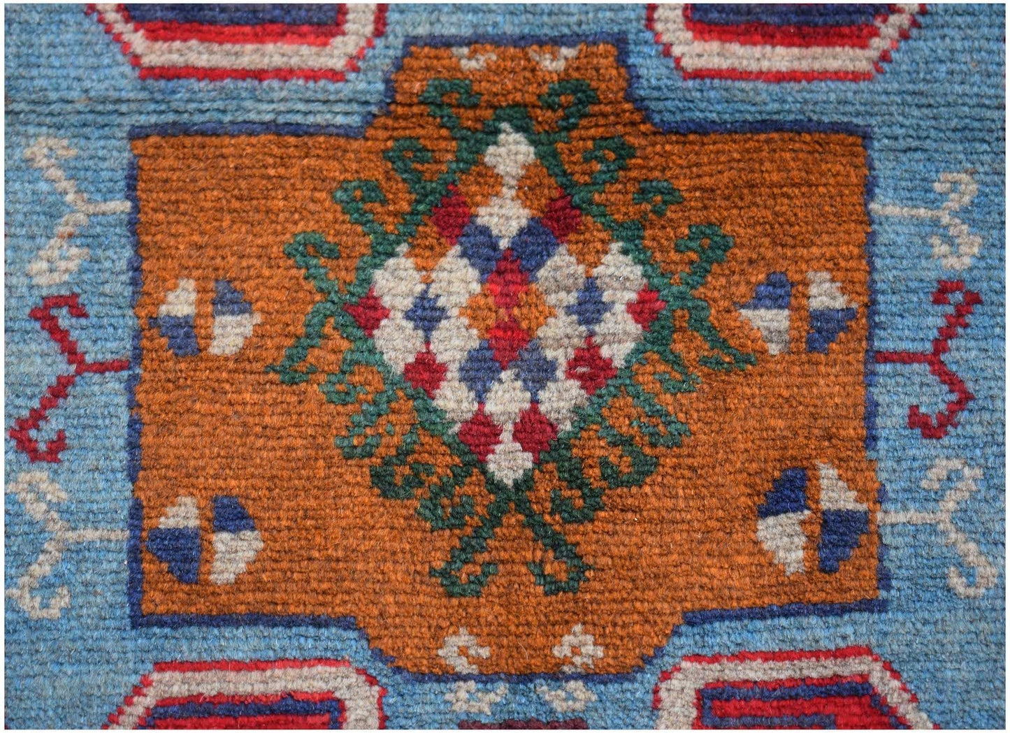 Handmade Afghan Pashm rug featuring a geometric floral motif in orange, blue, and ivory wool.