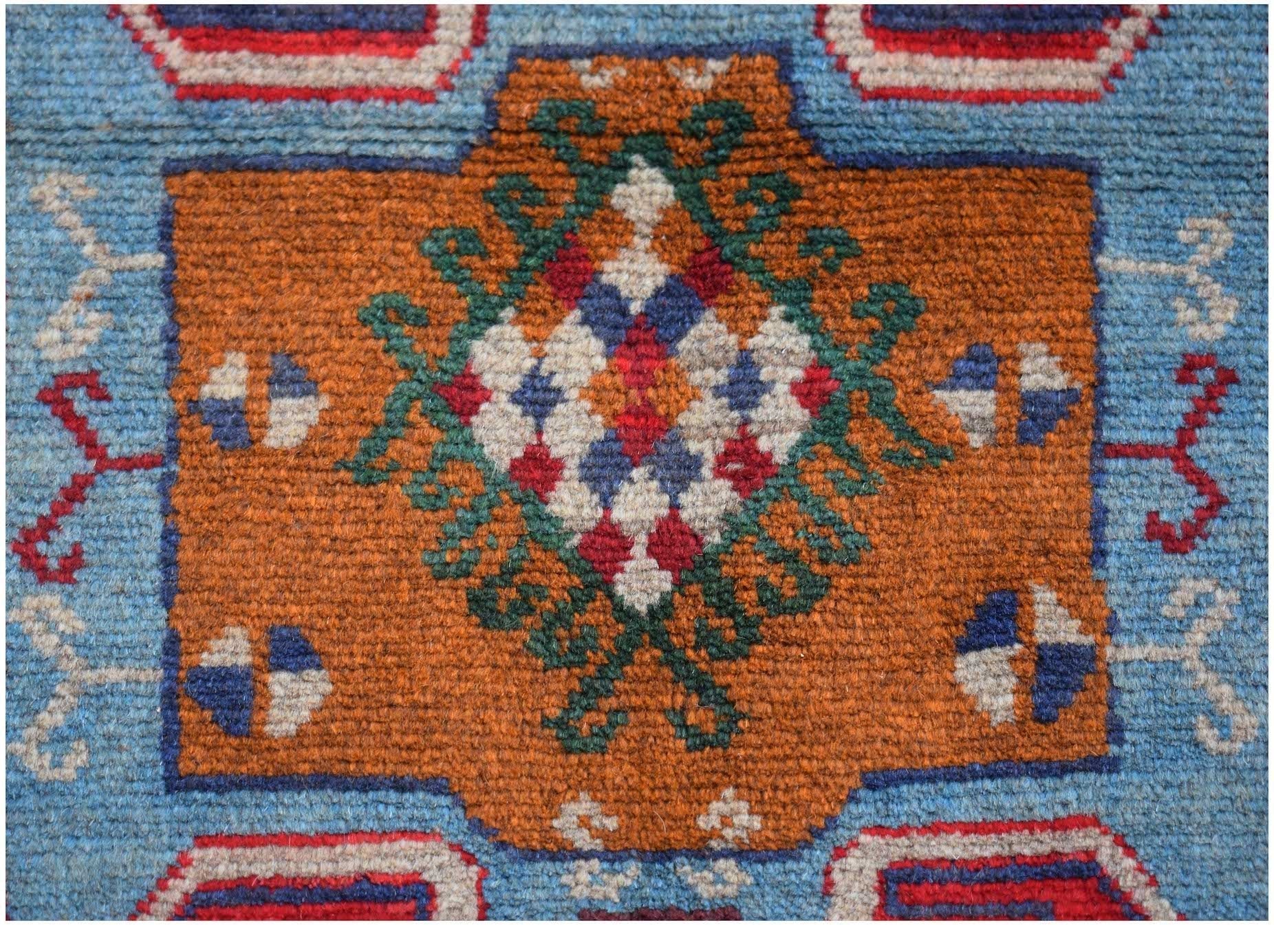 Handmade Afghan Pashm rug featuring a geometric floral motif in orange, blue, and ivory wool.