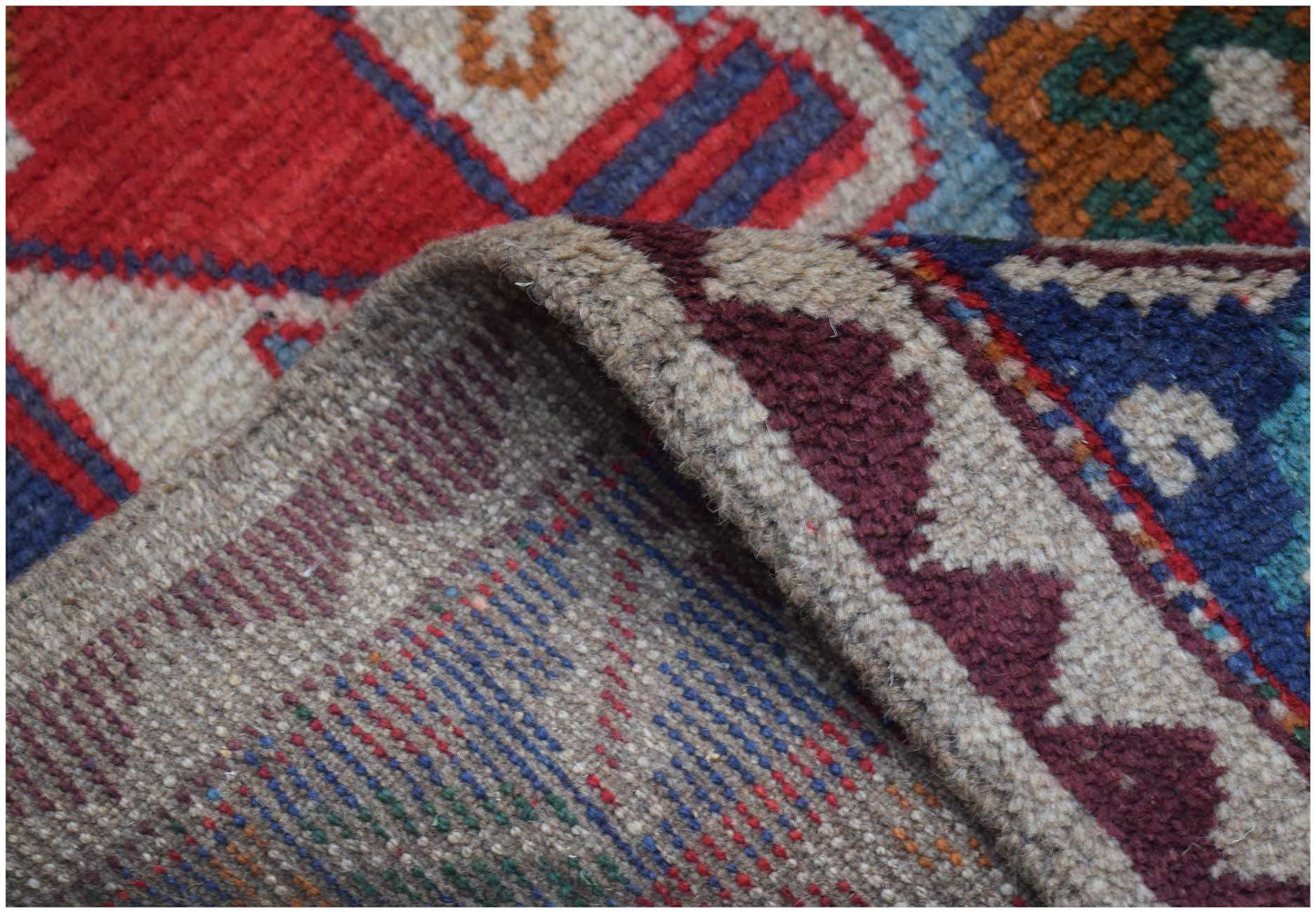 A close-up view of a handmade Afghan Pashm rug showing its wool texture and colorful tribal pattern.