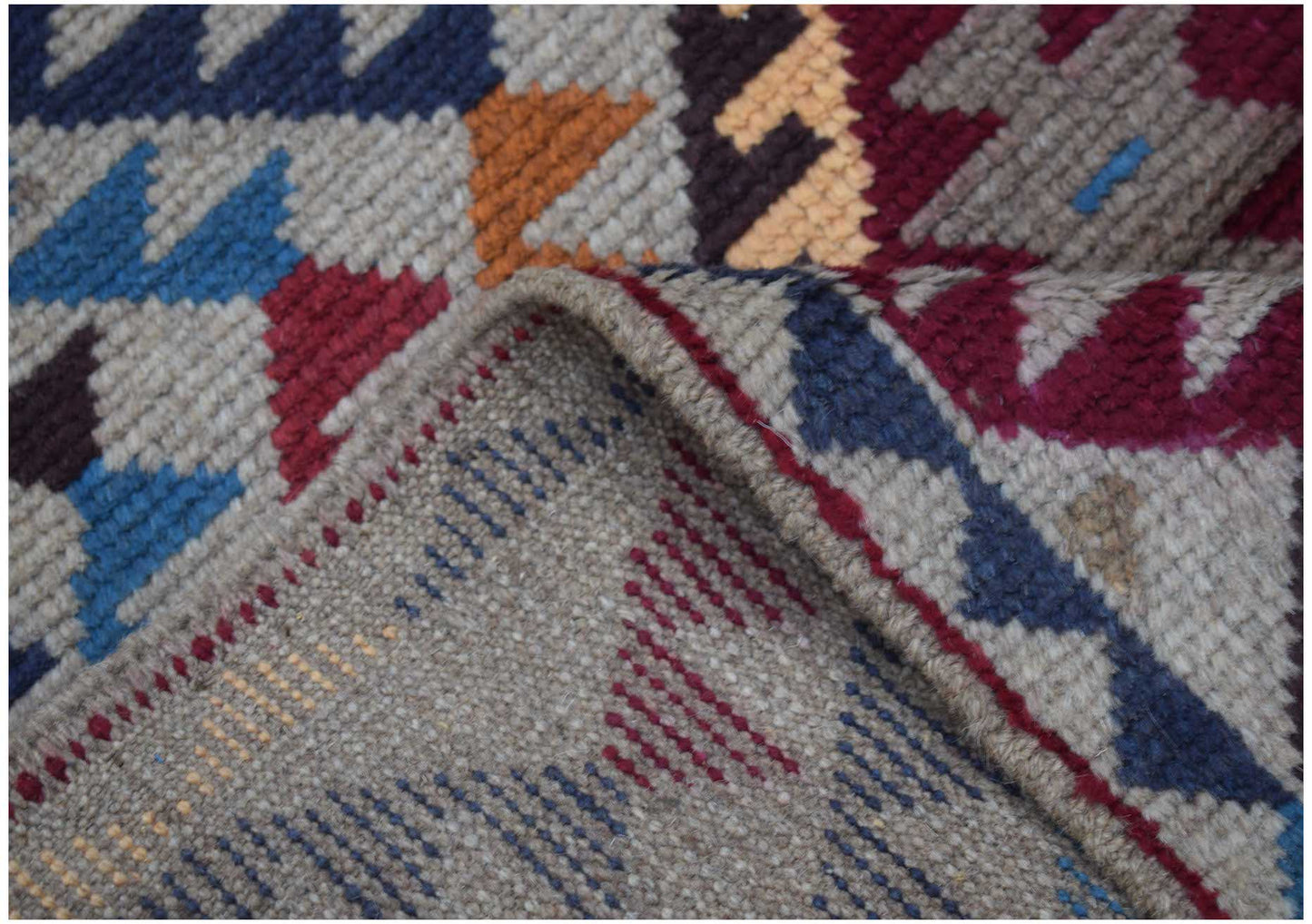 A handmade Afghan Pashm rug featuring a geometric tribal pattern in red, blue, and ivory wool.