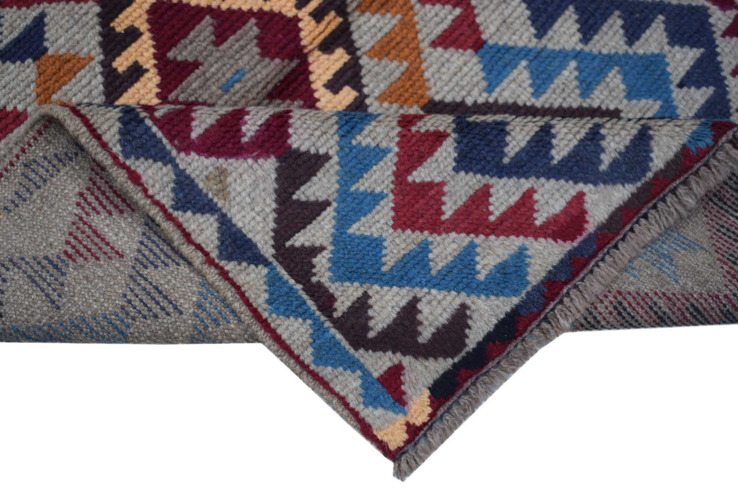 A handmade Afghan Pashm rug featuring a geometric tribal pattern in red, blue, and brown tones.