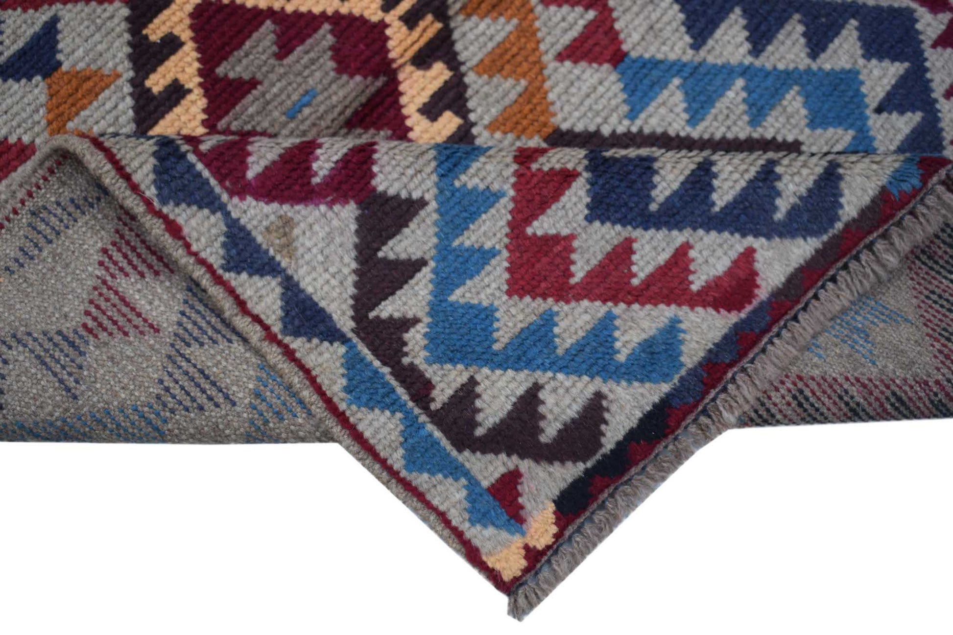 A handmade Afghan Pashm rug featuring a geometric tribal pattern in red, blue, and brown tones.