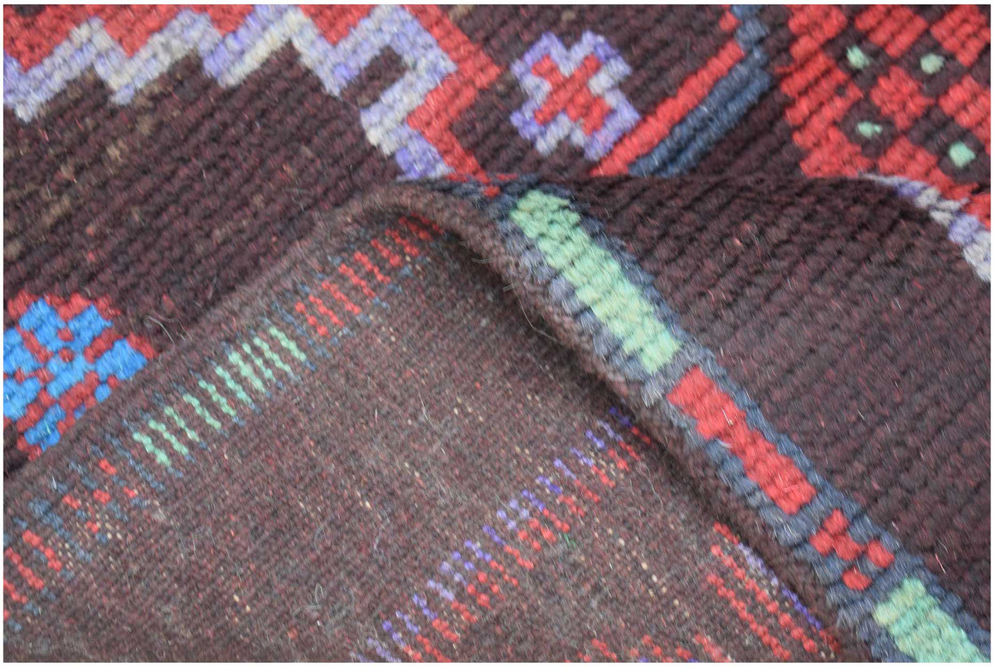 A close-up view of a handmade Afghan Pashm rug featuring dark wool with geometric patterns.