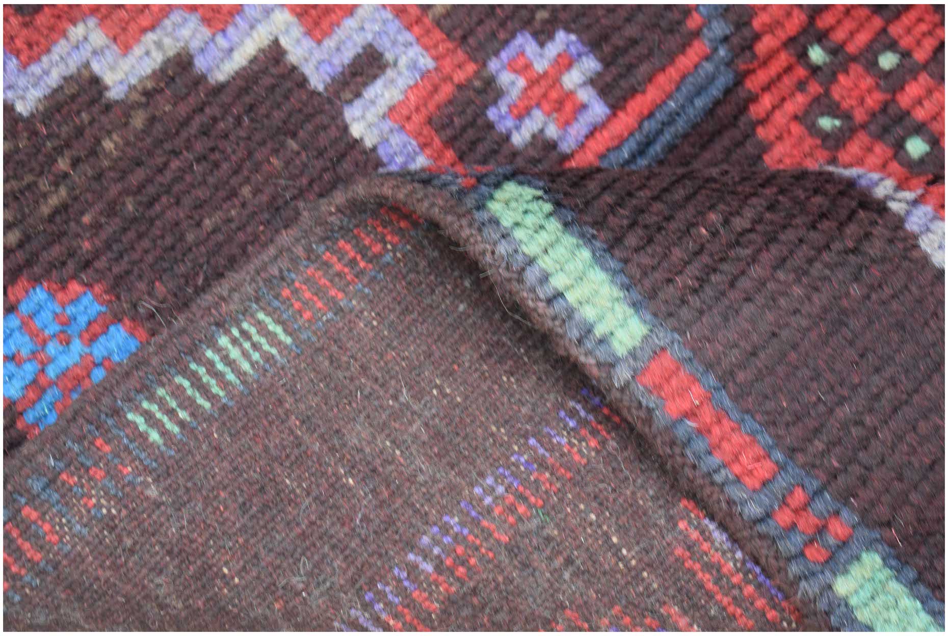 A close-up view of a handmade Afghan Pashm rug featuring dark wool with geometric patterns.