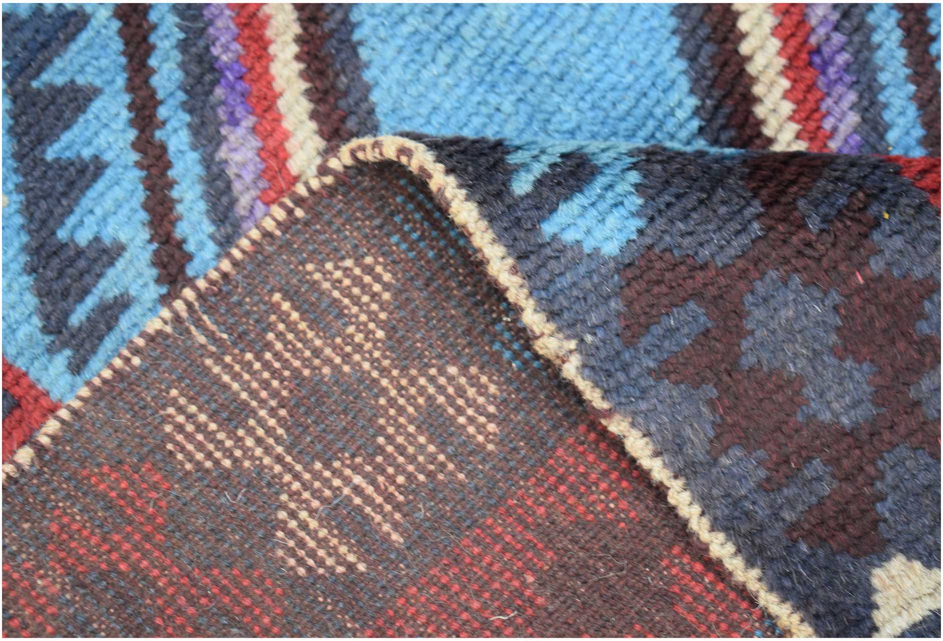 A handmade Afghan Pashm rug featuring a geometric pattern in shades of blue, red, and brown.