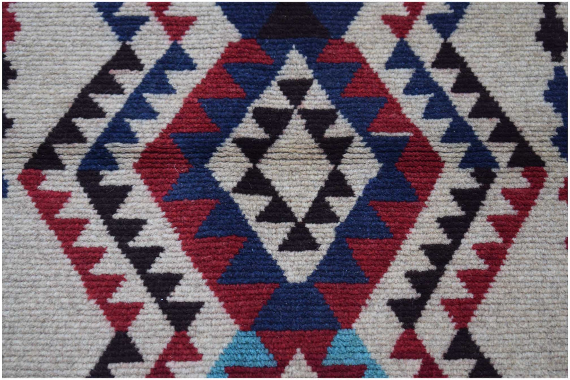 Handmade Afghan Pashm rug featuring a geometric diamond pattern in red, blue, and ivory wool.