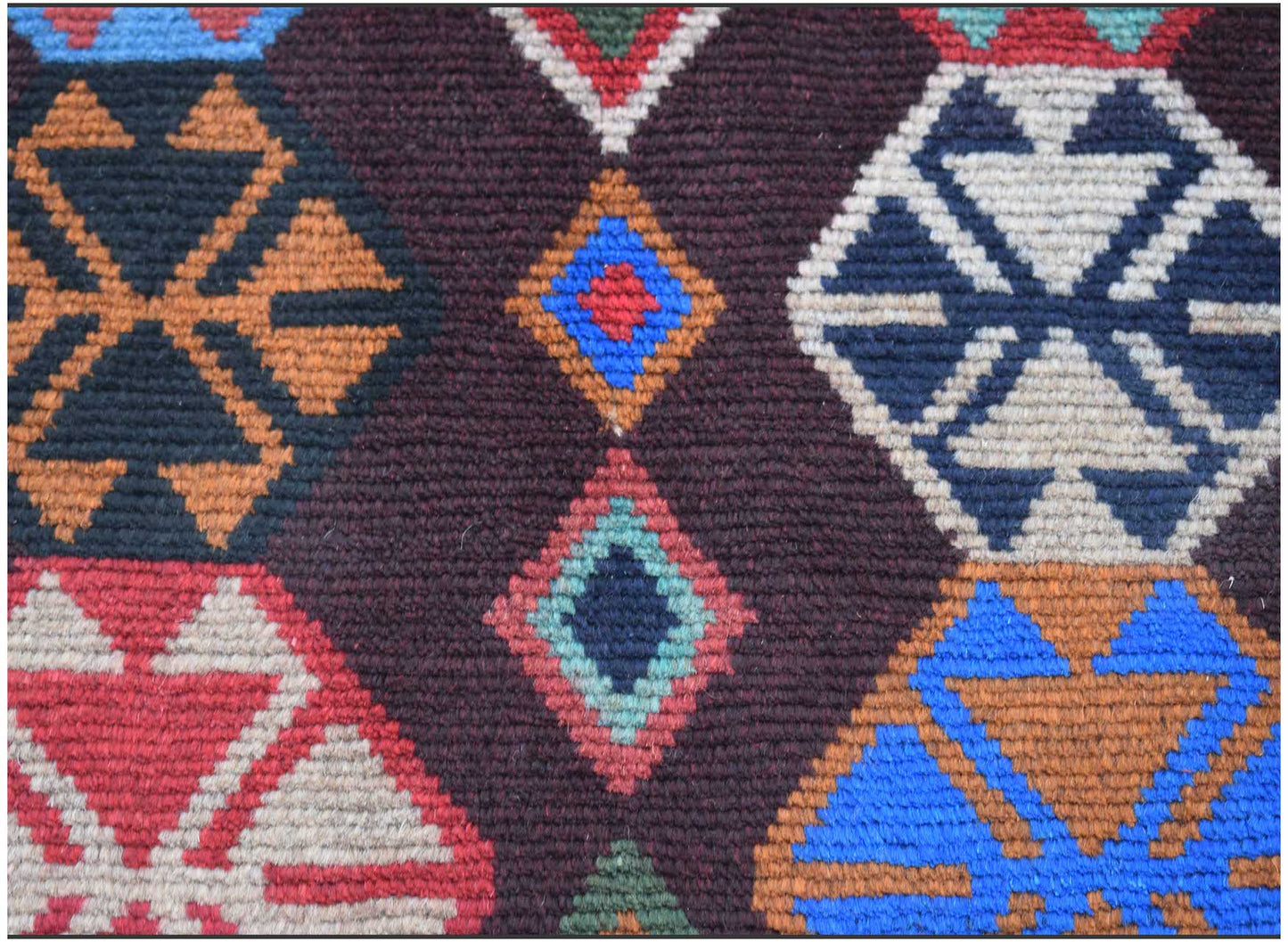 A handmade Afghan Pashm rug featuring a geometric pattern of diamonds in blue, red, and ivory.