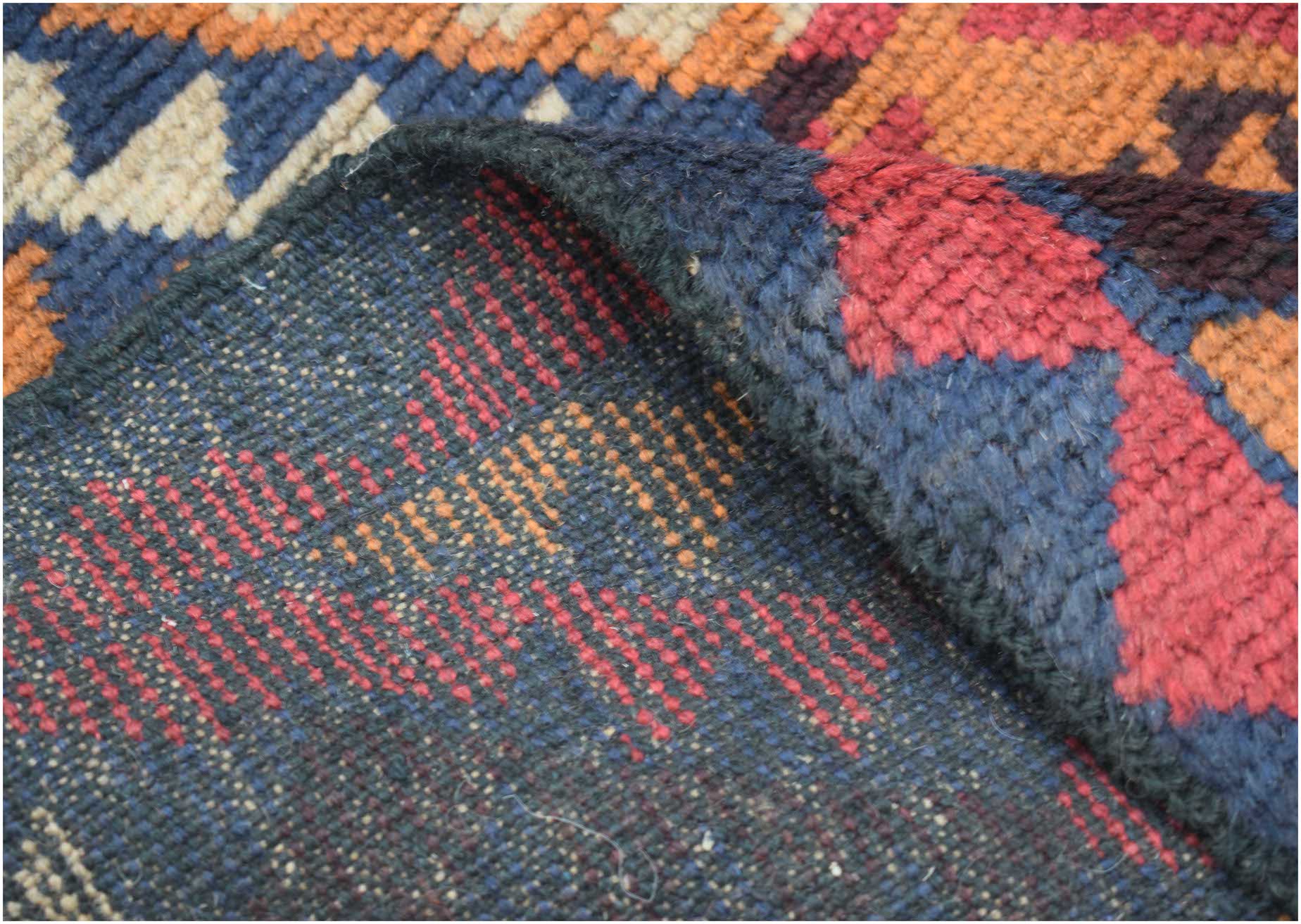 A corner of a handmade Afghan Pashm rug showing its dark red, blue, and ivory geometric pattern.