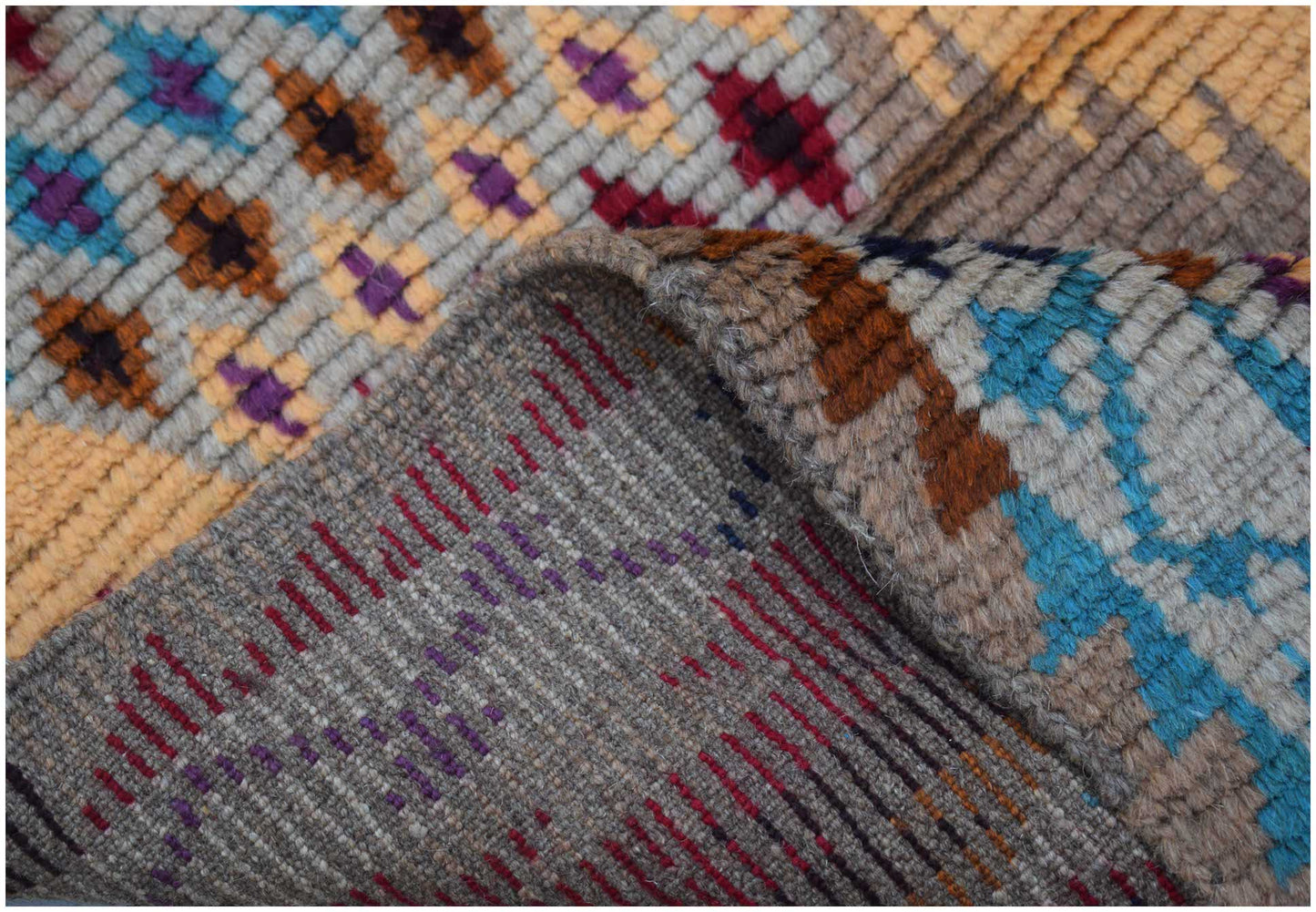 A handmade Afghan Pashm rug featuring a geometric pattern in blue, red, brown, and ivory wool.