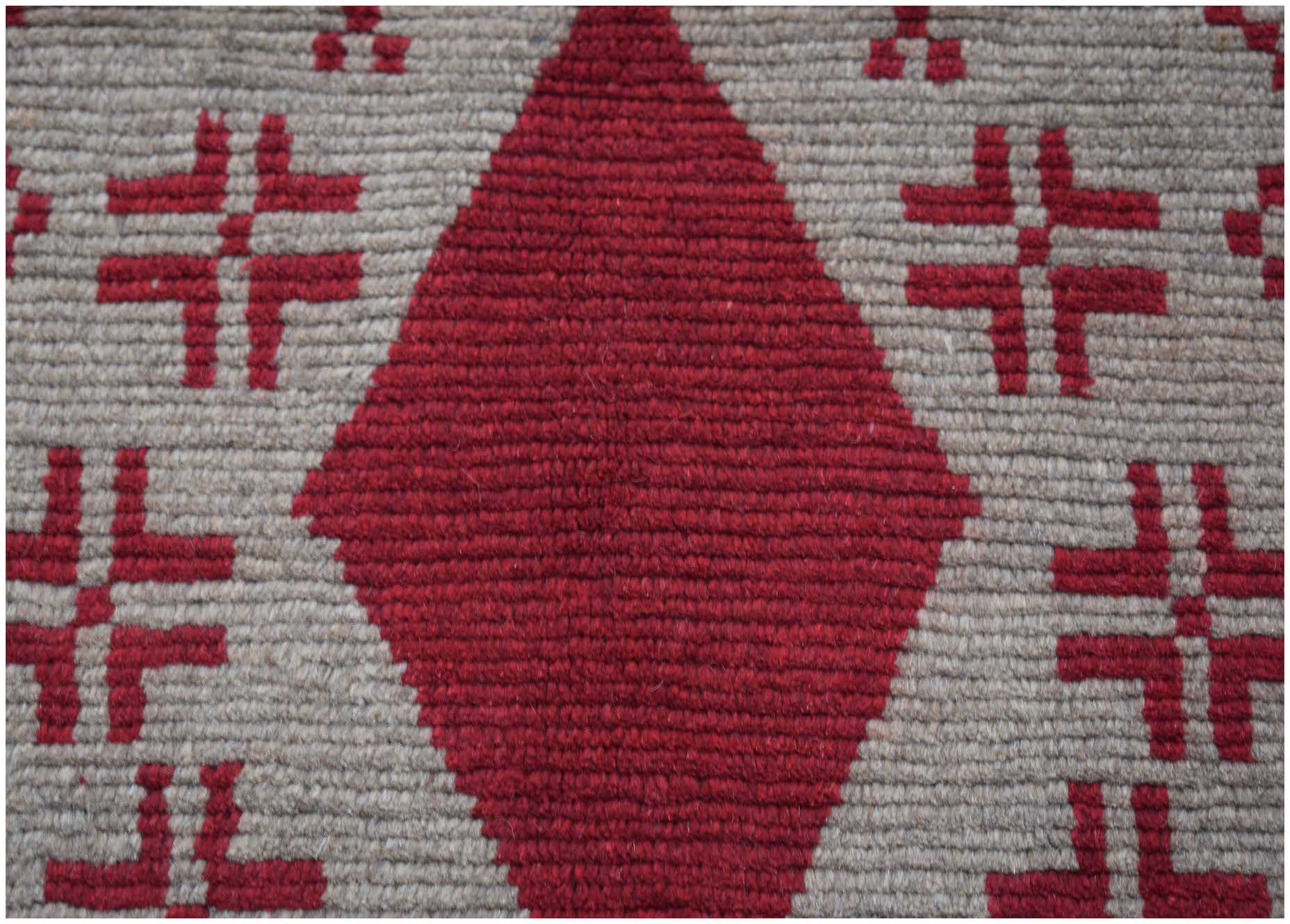 Handmade Afghan Pashm rug featuring a large red diamond pattern on a textured beige wool background.