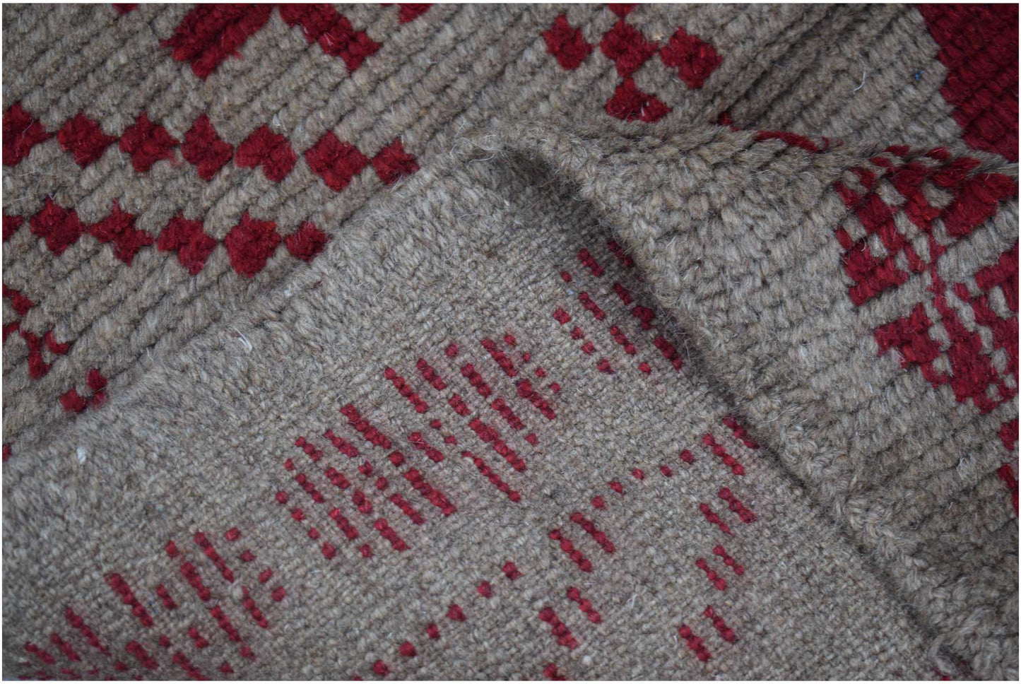 A handmade Afghan Pashm rug featuring a geometric pattern in deep red on a textured brown wool base.