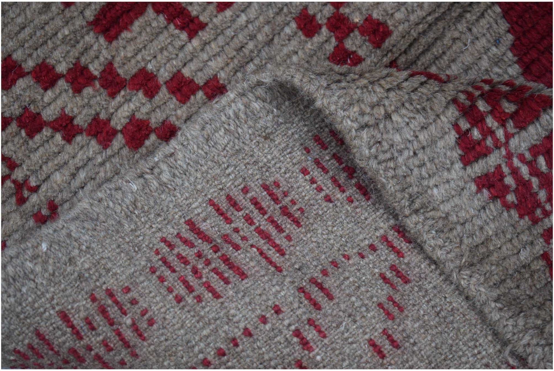 A handmade Afghan Pashm rug featuring a geometric pattern in deep red on a textured brown wool base.
