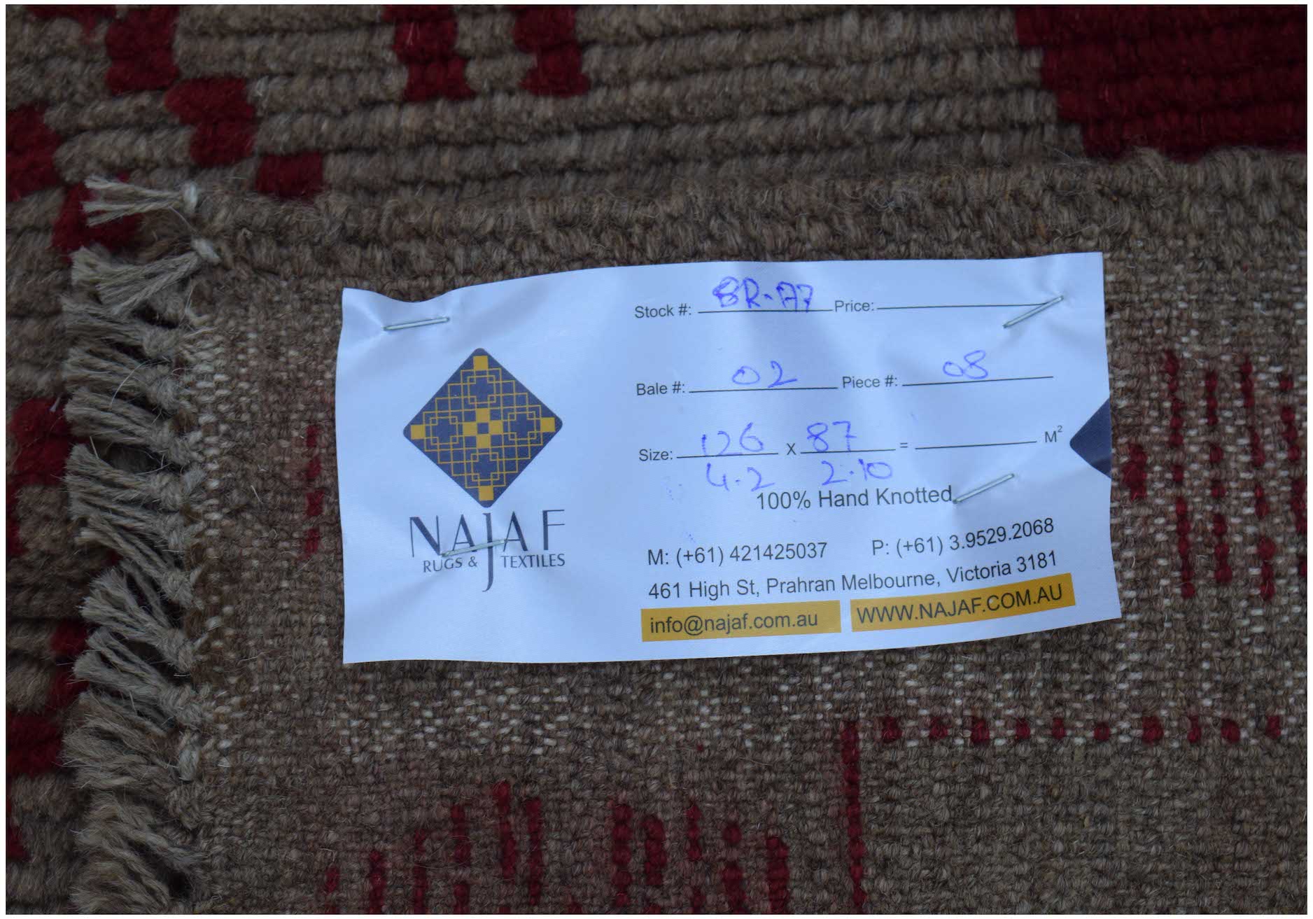 A handmade Afghan Pashm rug featuring a geometric pattern in dark red and brown wool.