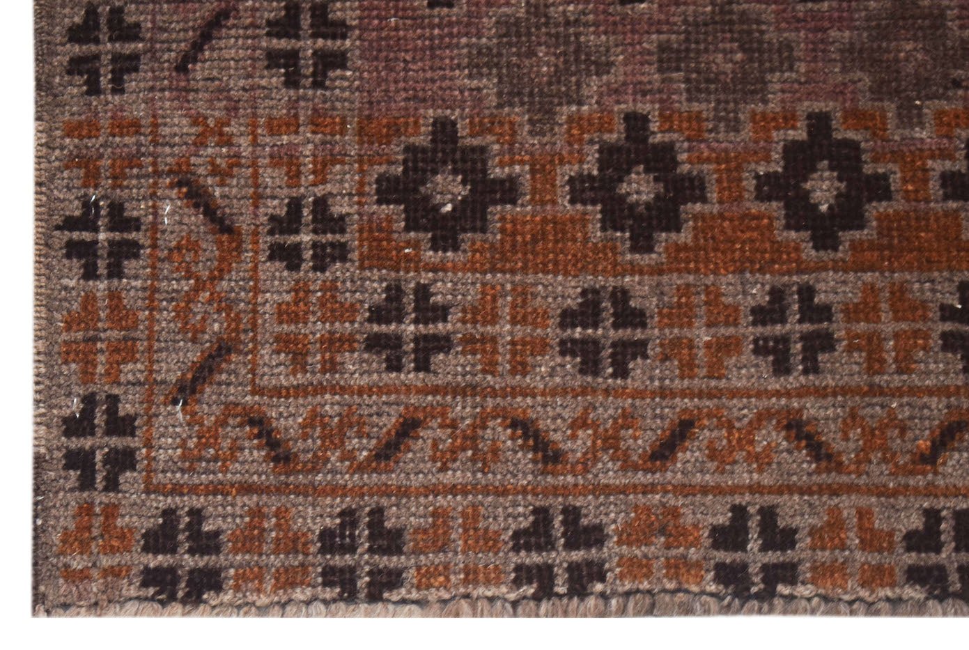 A close-up of a vintage Afghan Baluch rug featuring geometric patterns in brown and rust tones.