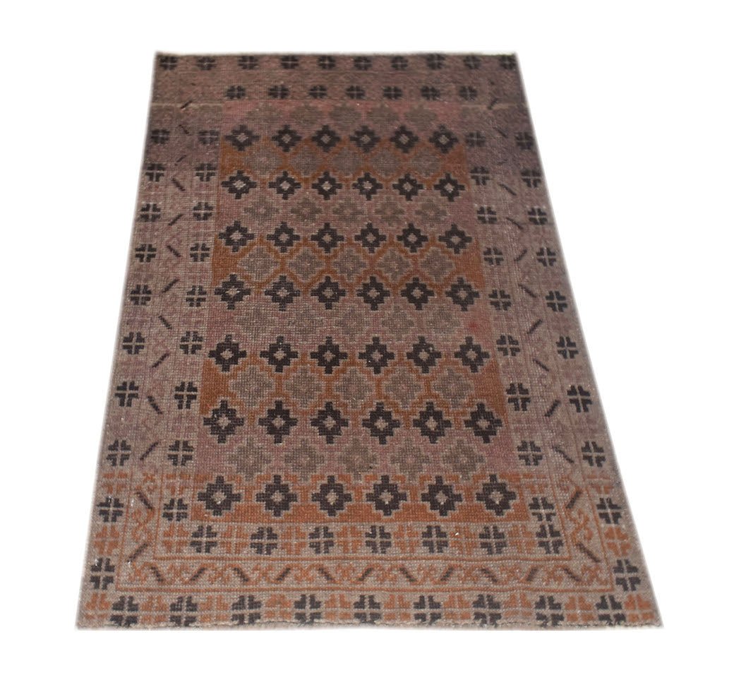 A vintage handmade Afghan Baluch rug featuring a geometric pattern in shades of brown and pink.
