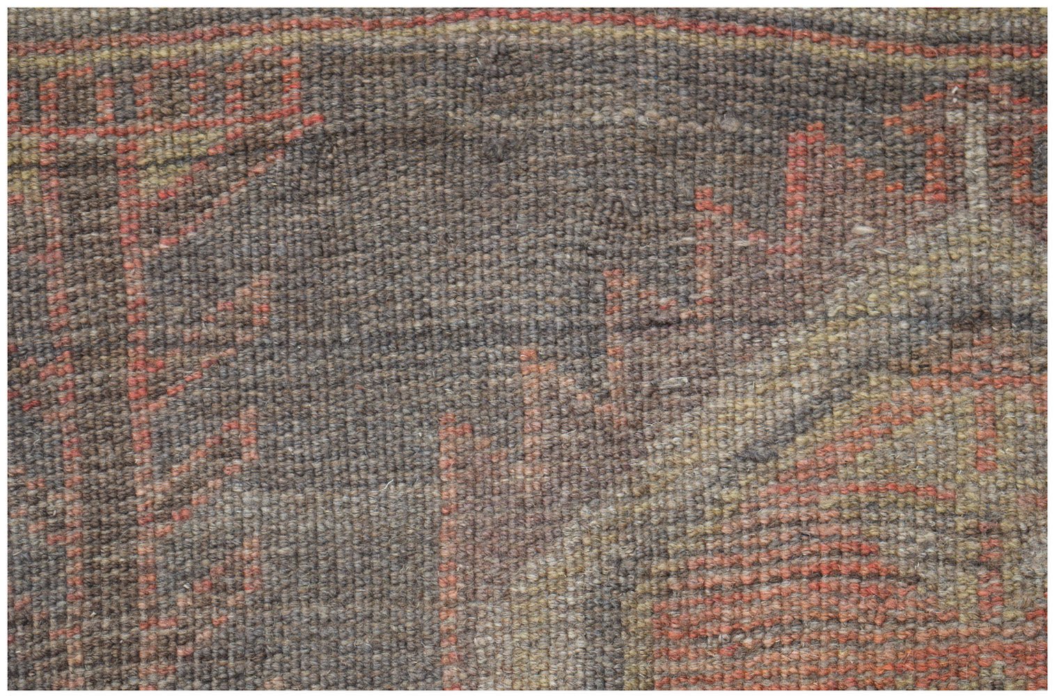 A close-up of a handmade Afghan Baluch rug featuring geometric patterns in red, brown, and tan.