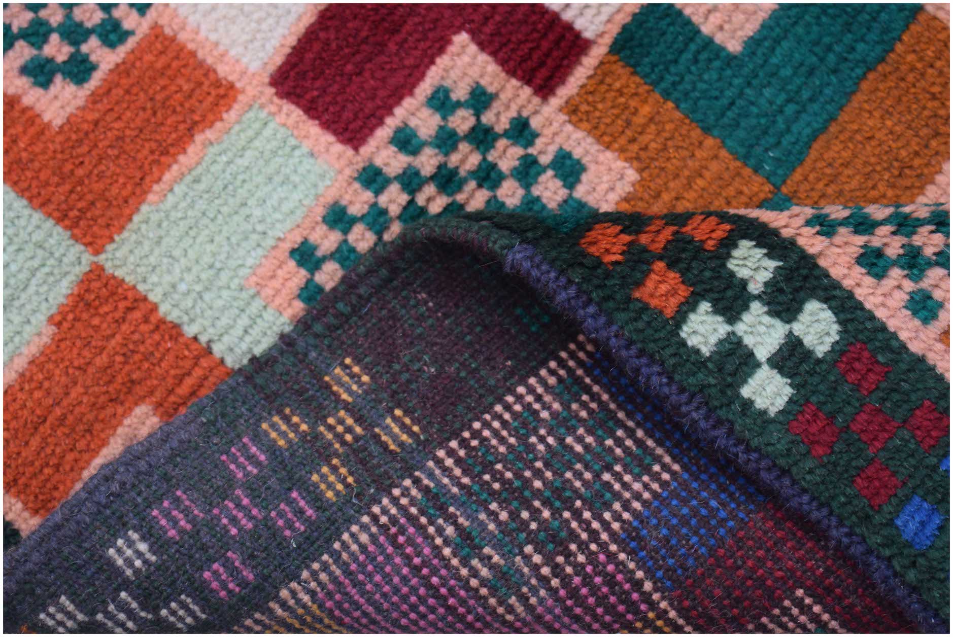 A handmade Afghan Pashm rug featuring a colorful geometric grid pattern and a dark wool backing.