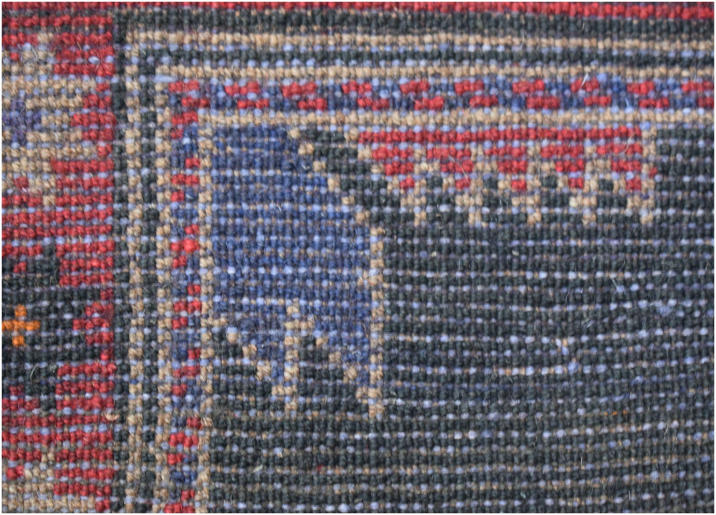 A close-up of a handmade Afghan Baluch rug featuring intricate geometric patterns in red and blue.