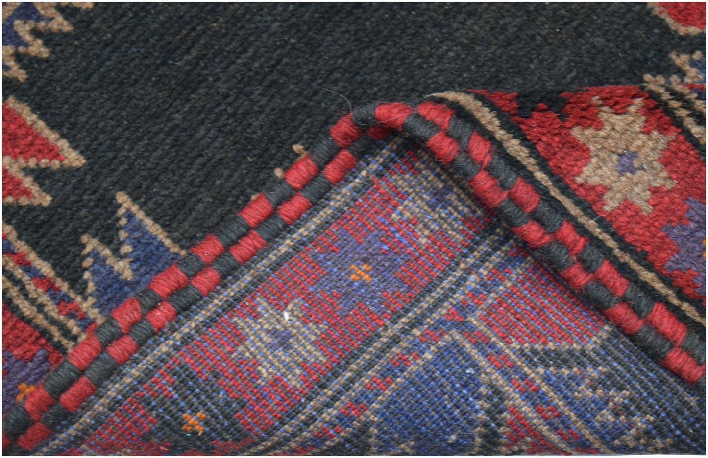 A corner of a handmade Afghan Baluch rug showing its dark wool pile and intricate woven underside.