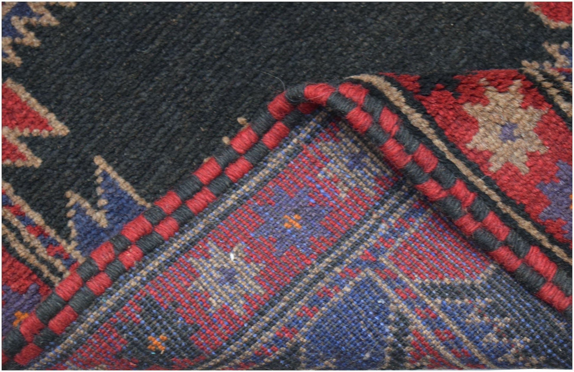 A corner of a handmade Afghan Baluch rug showing its dark wool pile and intricate woven underside.